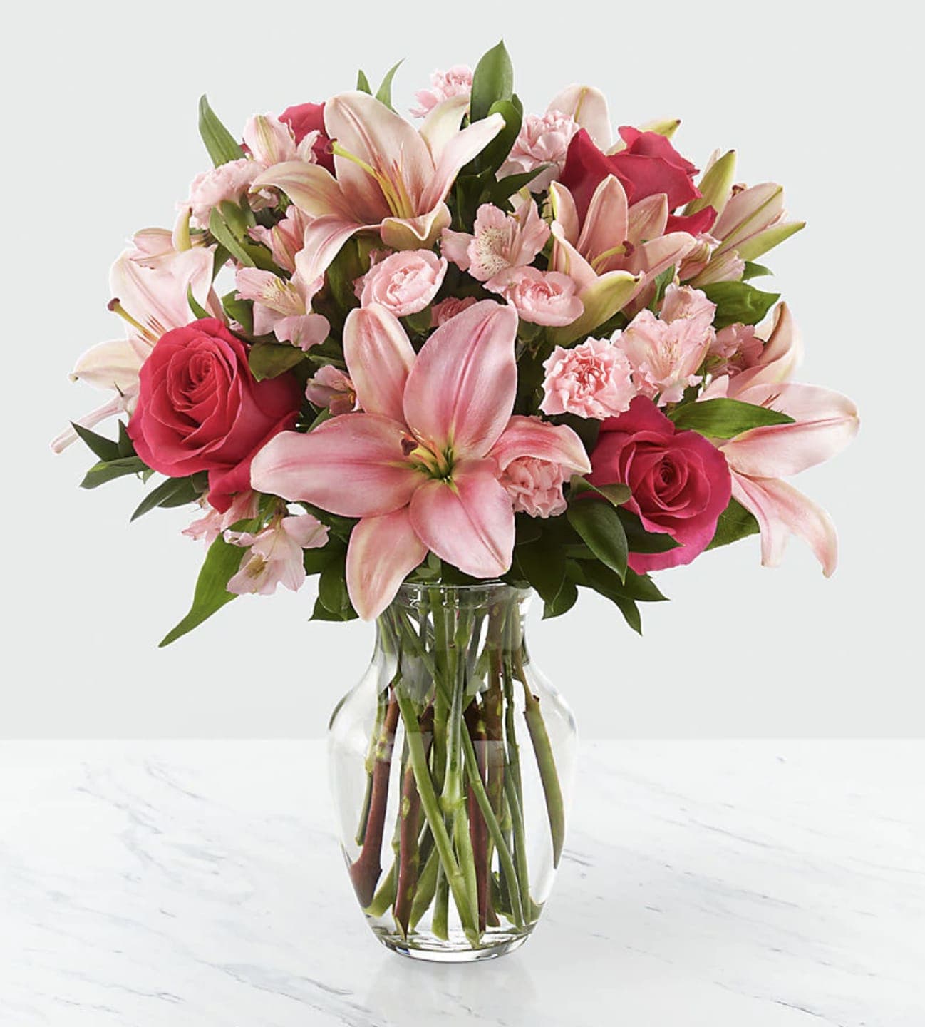 Pink lilies, roses, and carnations in a clear glass vase