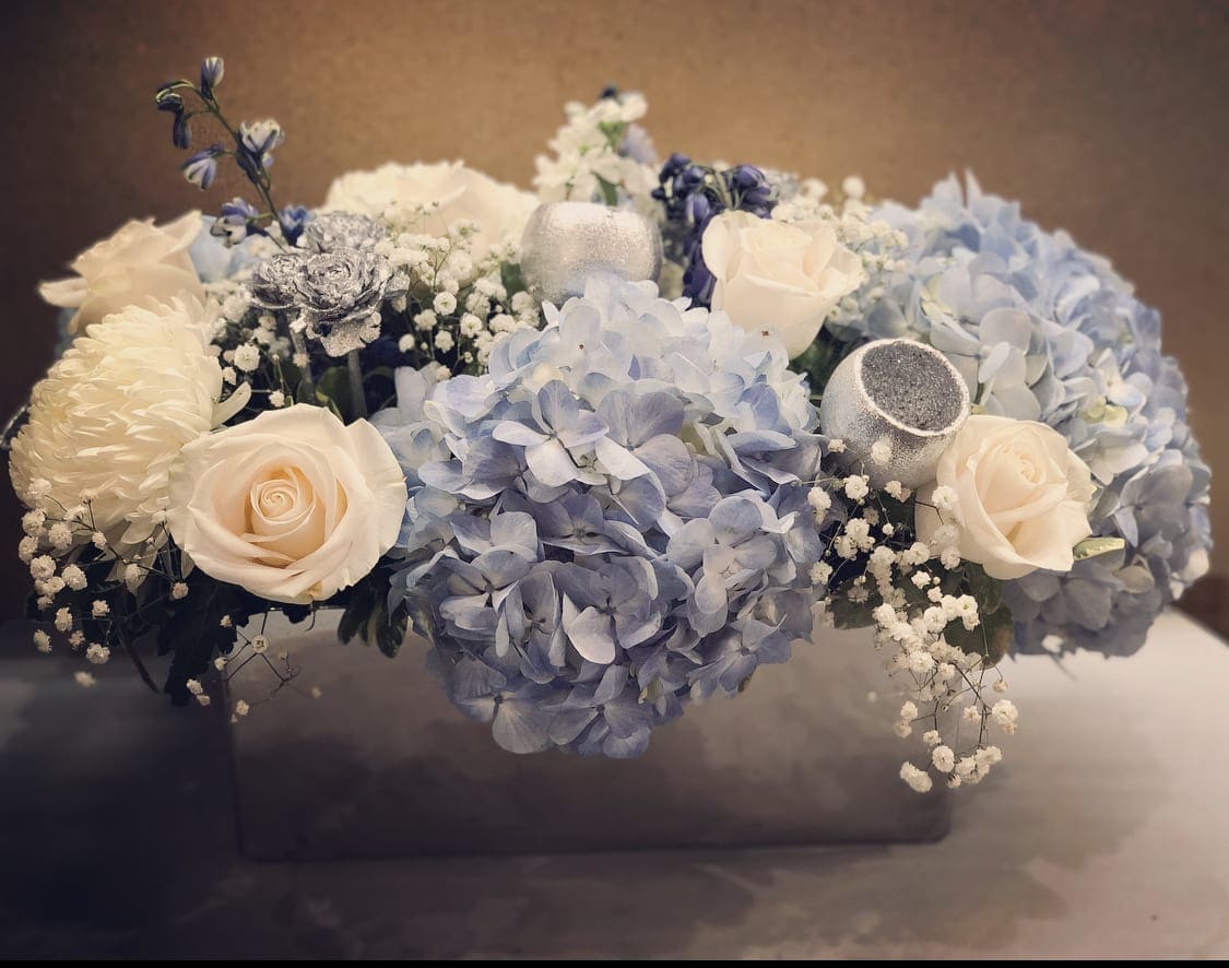 Blue hydrangeas and cream roses arranged in a low box