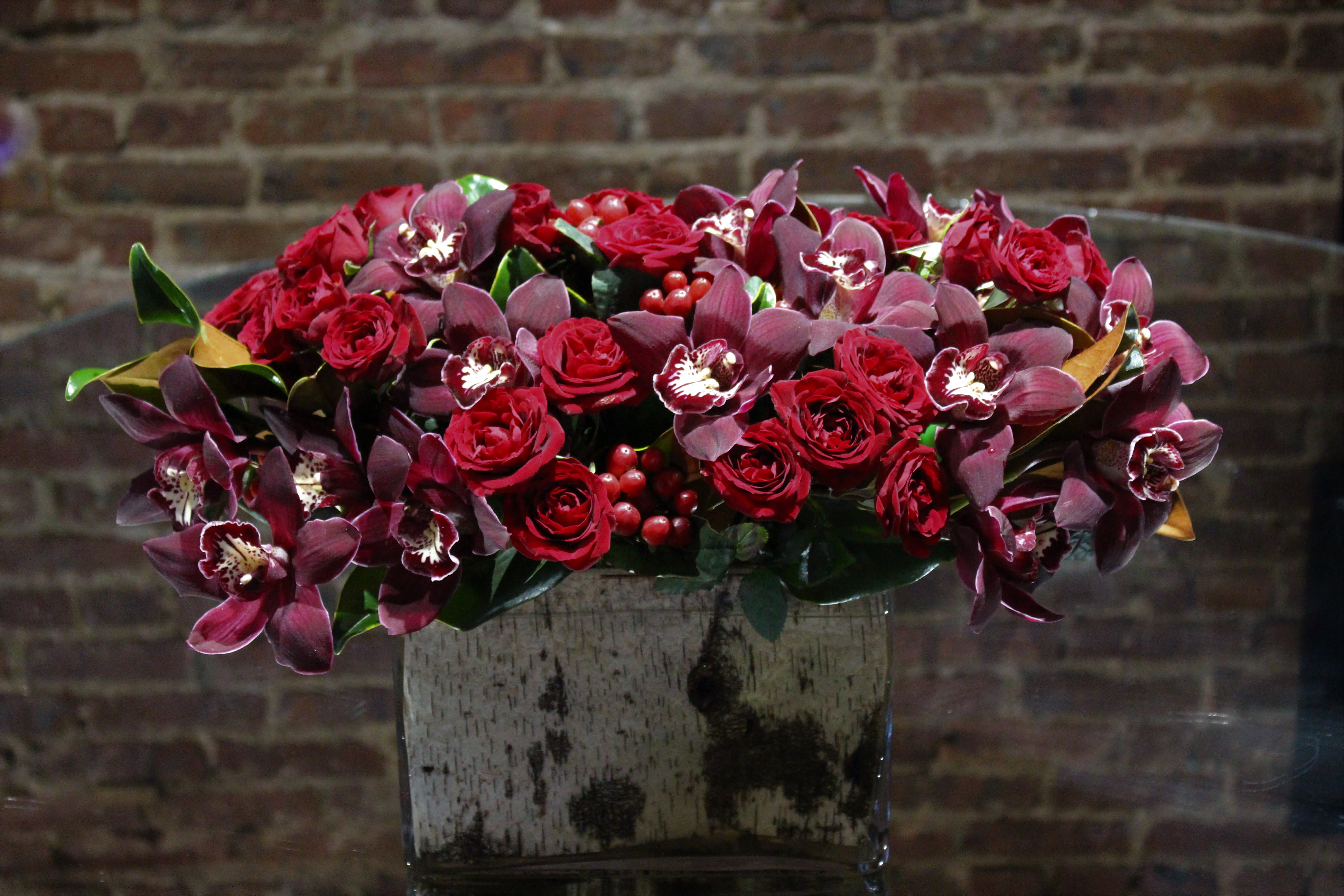 Red roses and burgundy orchids arranged in a square vase