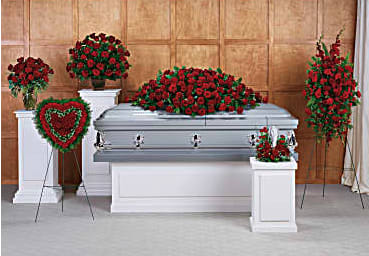 Casket surrounded by red rose funeral sprays and a heart wreath