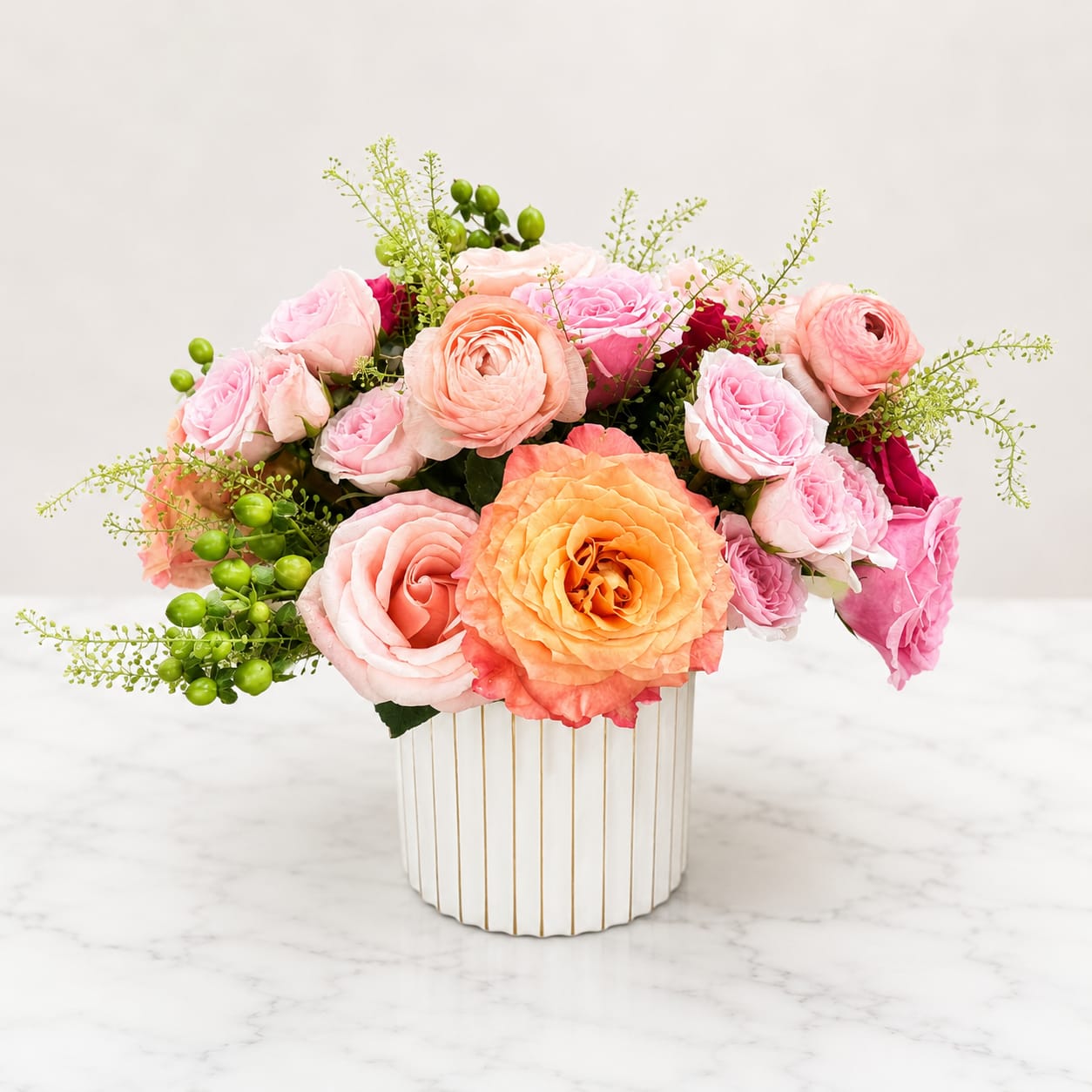 Peach Garden - A romantic garden style arrangement of premium peach and blush roses, ranunculus, spray roses, green berries, and delicate seasonal textures, designed in a modern white ceramic vase. Soft, graceful, and beautifully uplifting for any occasion.