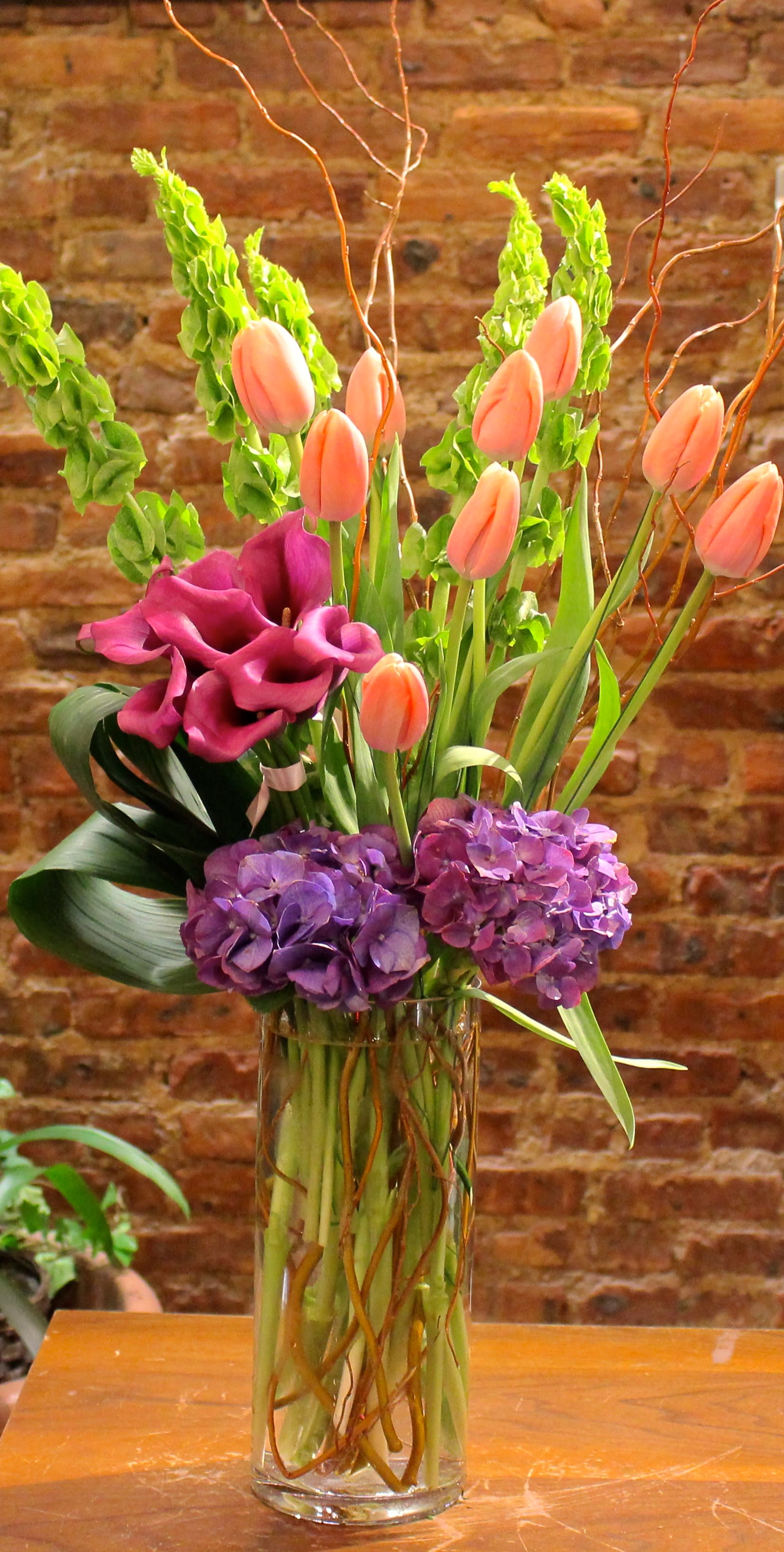 Tall vase arrangement with peach tulips, purple hydrangeas, and magenta calla lilies
