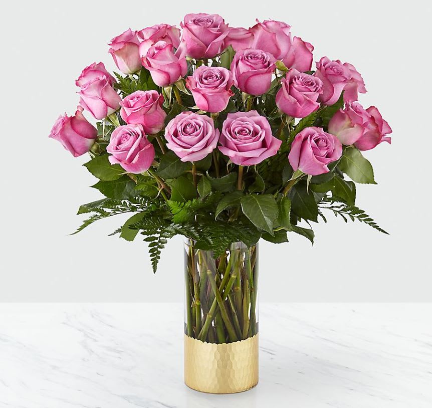 Pink roses arranged in a clear glass vase with a gold base