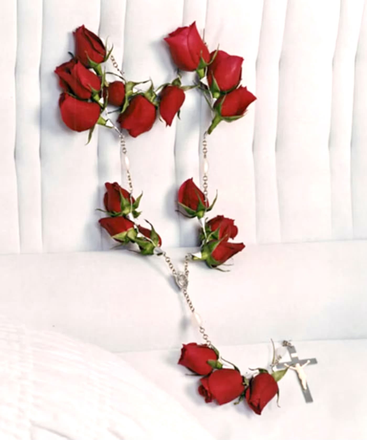 Red rose rosary with silver cross on white fabric