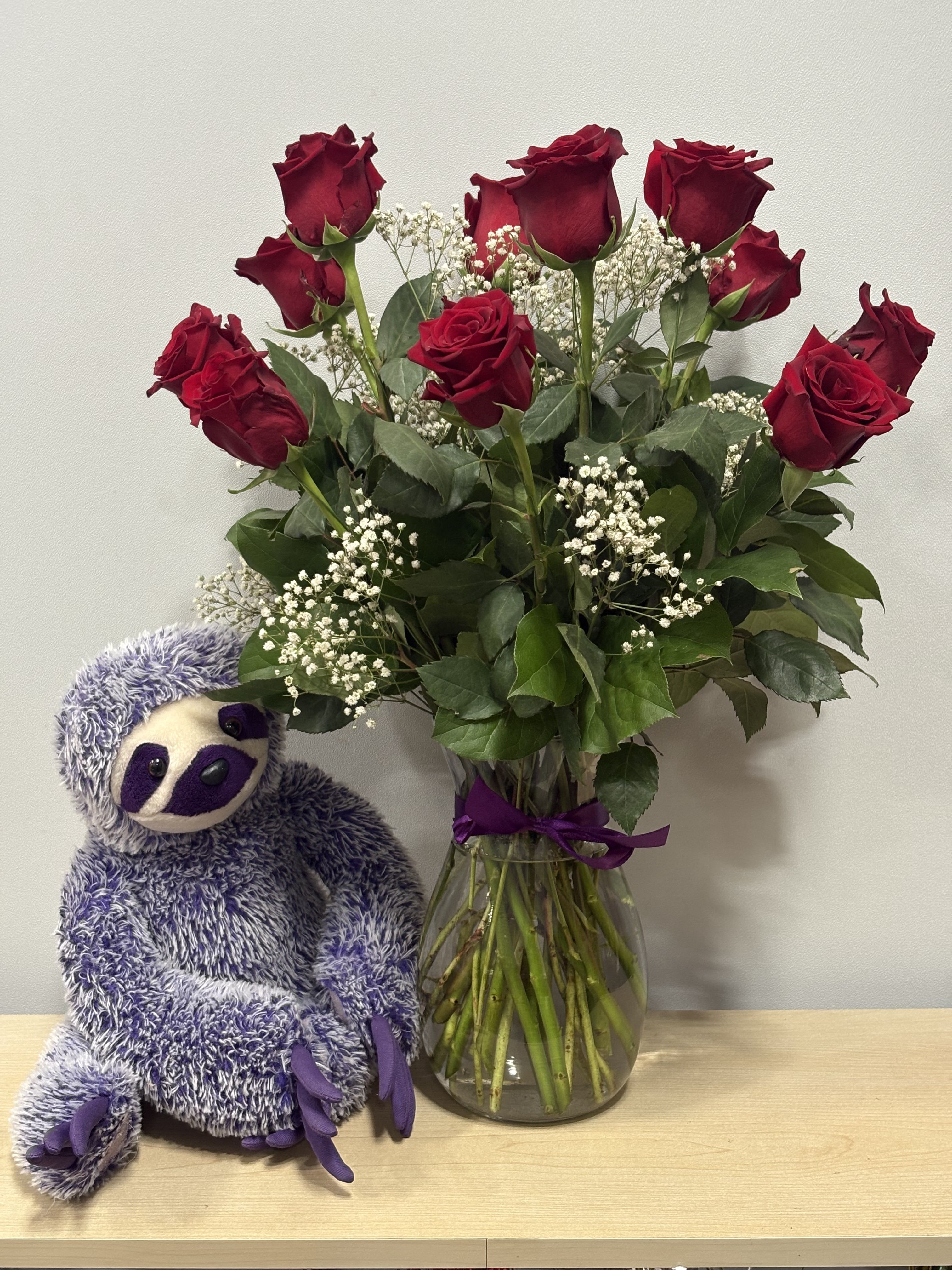 Bouquet of red roses in a glass vase beside a purple stuffed sloth