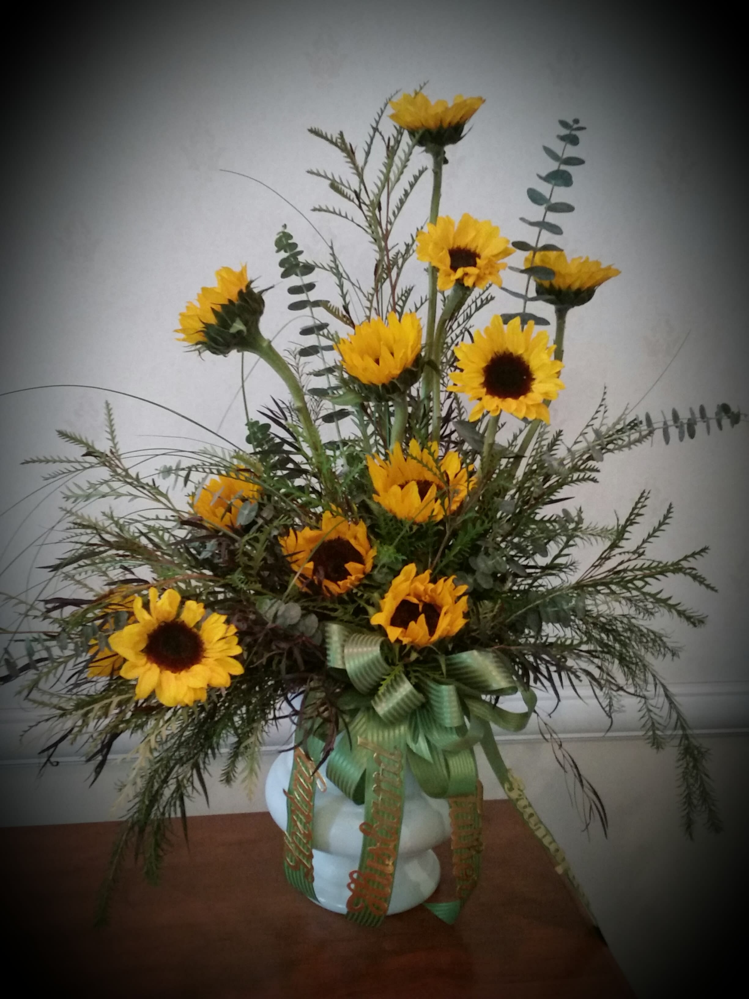 Tall sunflower arrangement in a white vase with green ribbon