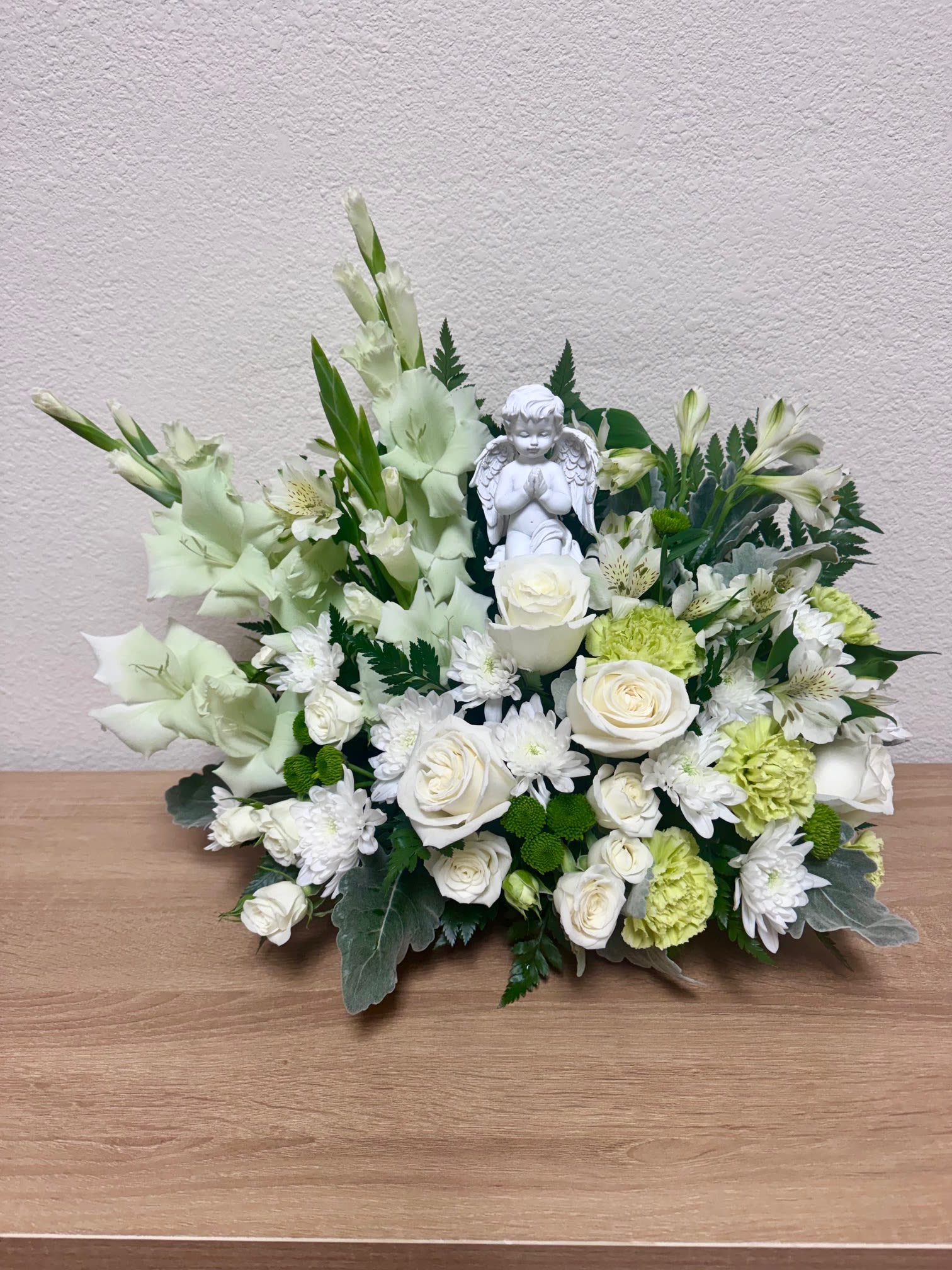 White floral arrangement with roses, chrysanthemums, and an angel figurine