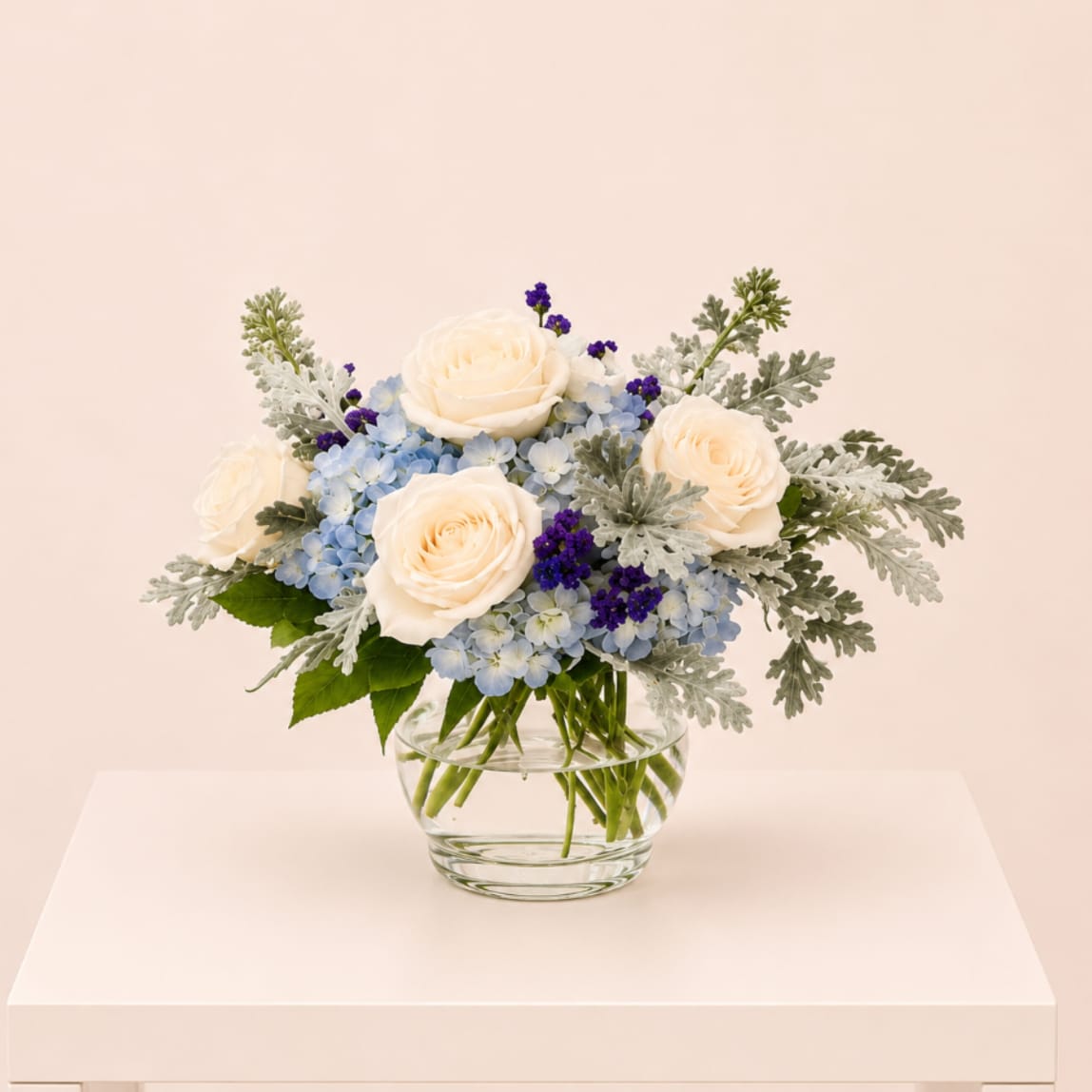 Cream roses and blue flowers in a clear glass vase