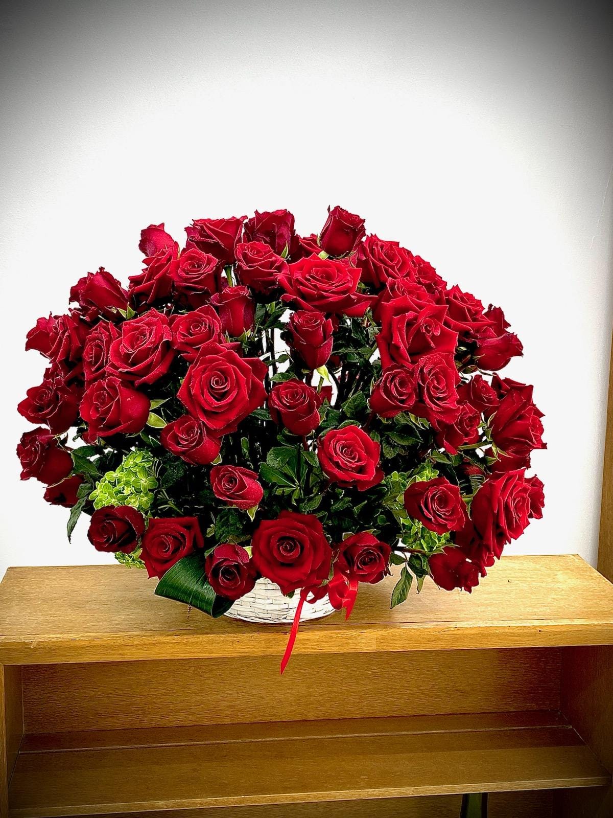 Large bouquet of red roses in a white basket with a red ribbon