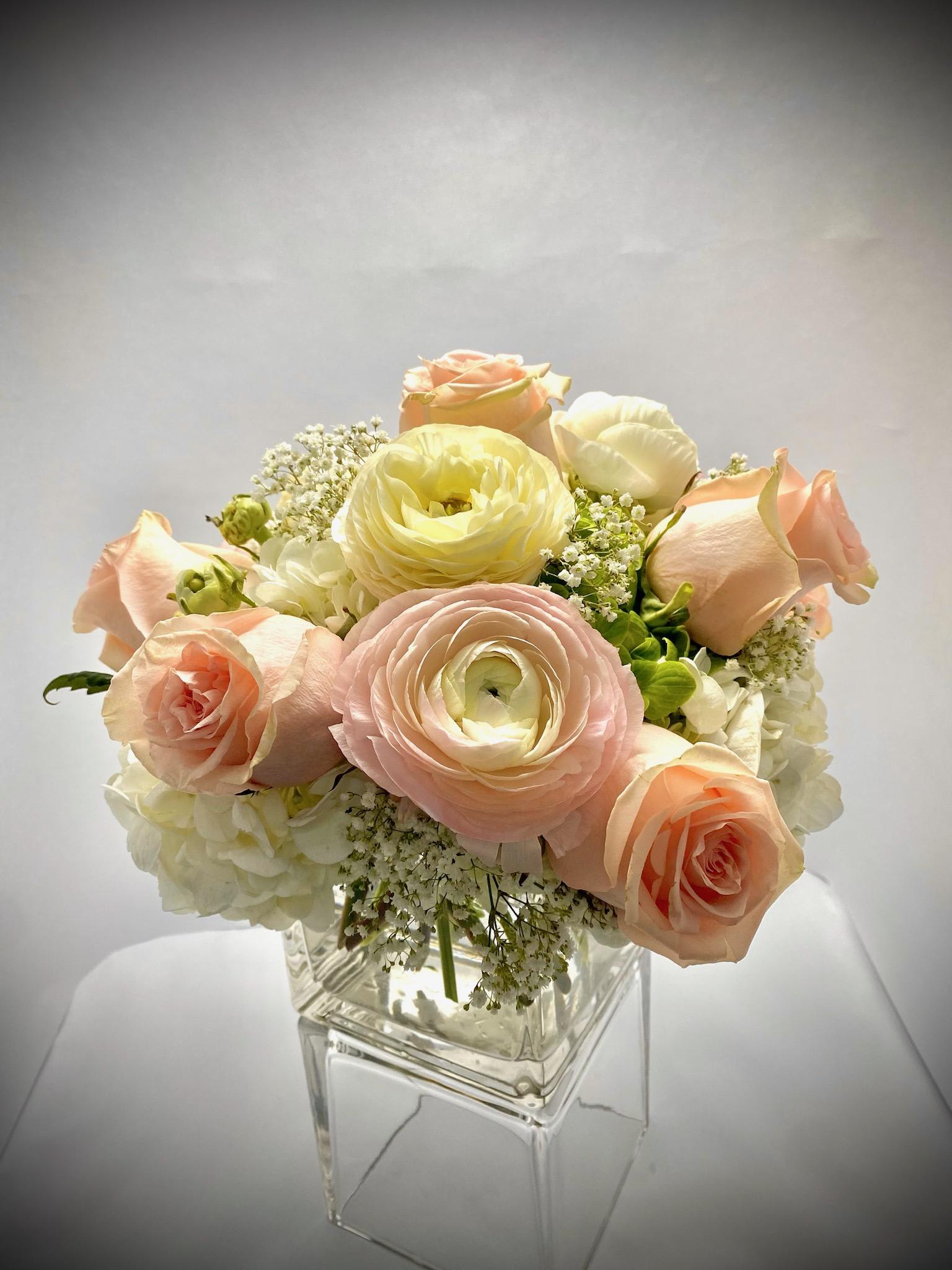 Pastel roses and ranunculus arranged in a clear glass vase