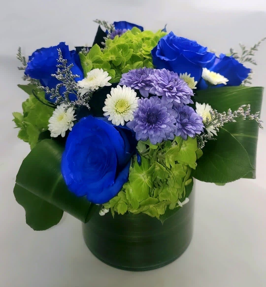 Blue roses and purple and white daisies in a green hatbox