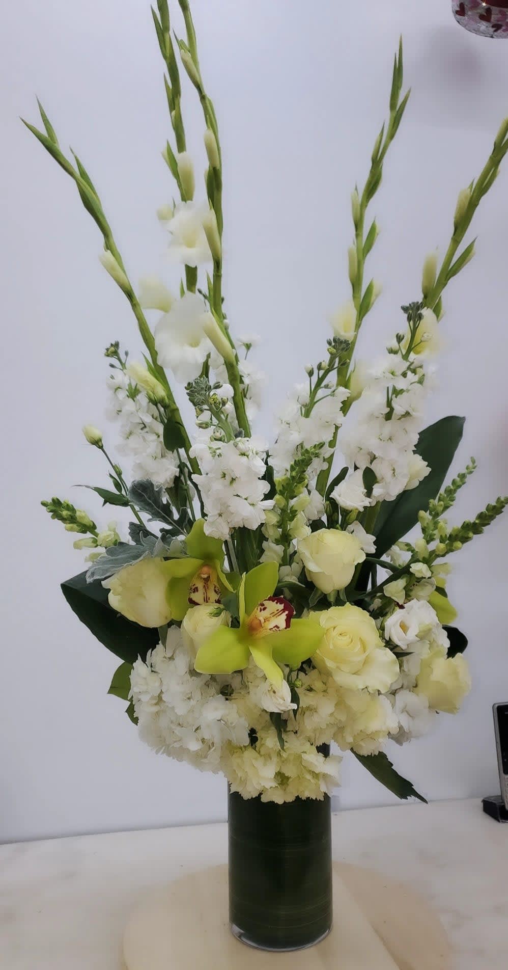 Tall white floral arrangement in a dark green vase with pale green orchids and roses