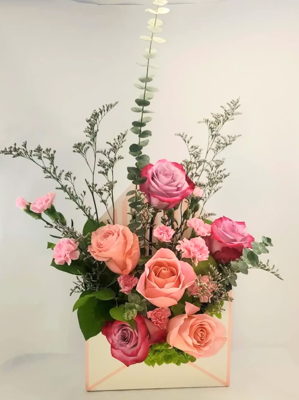 Pink and peach roses arranged in a pastel gift box with greenery
