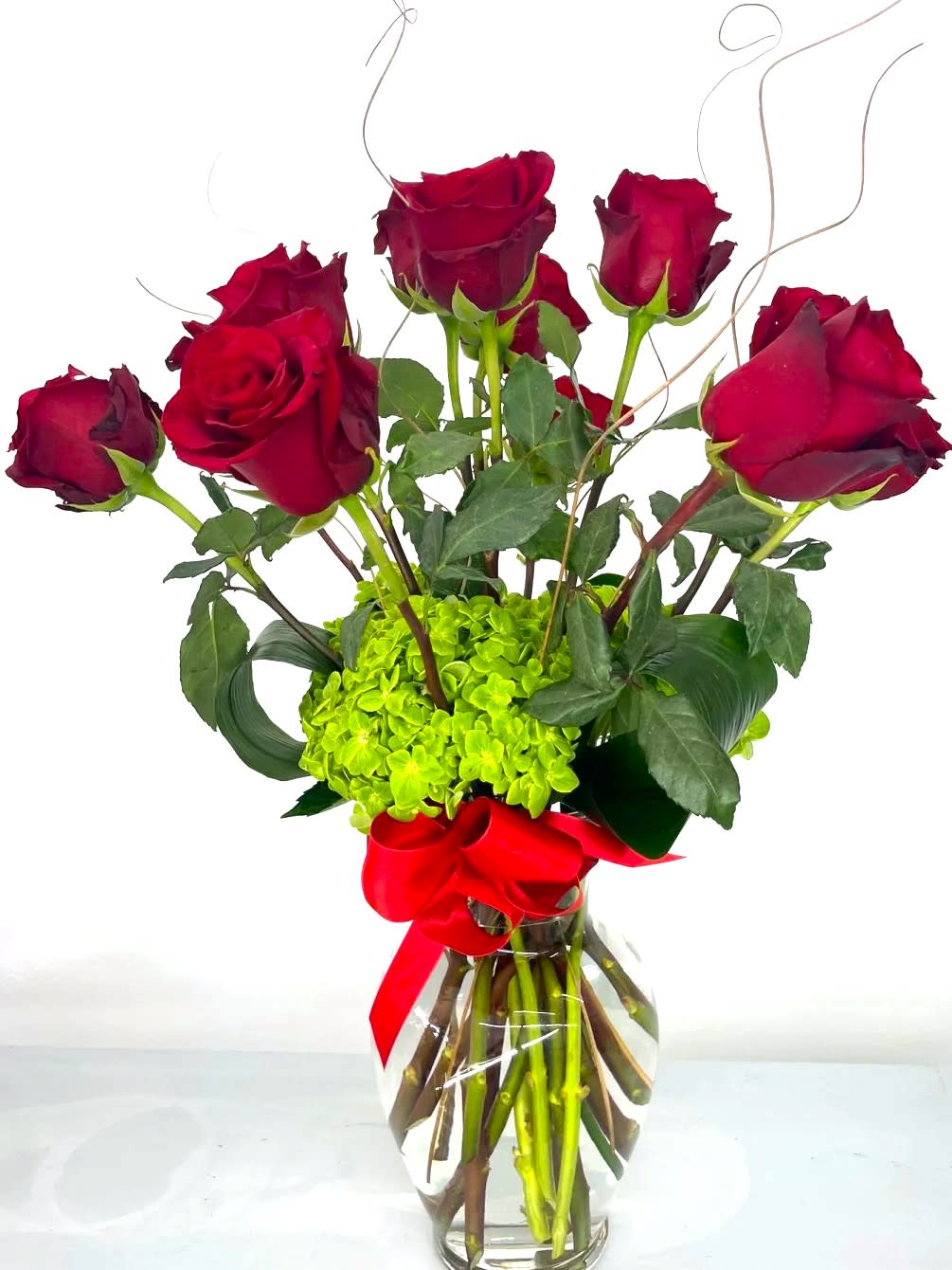 Red roses arranged in a clear glass vase with a red ribbon