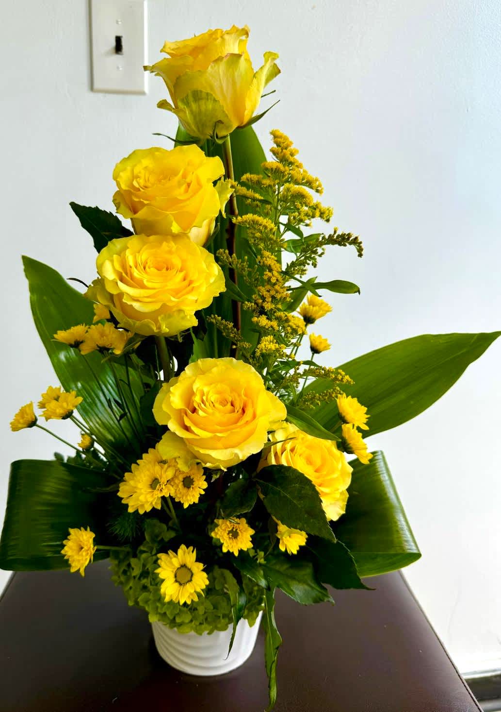 Yellow roses and small yellow daisies in a white vase