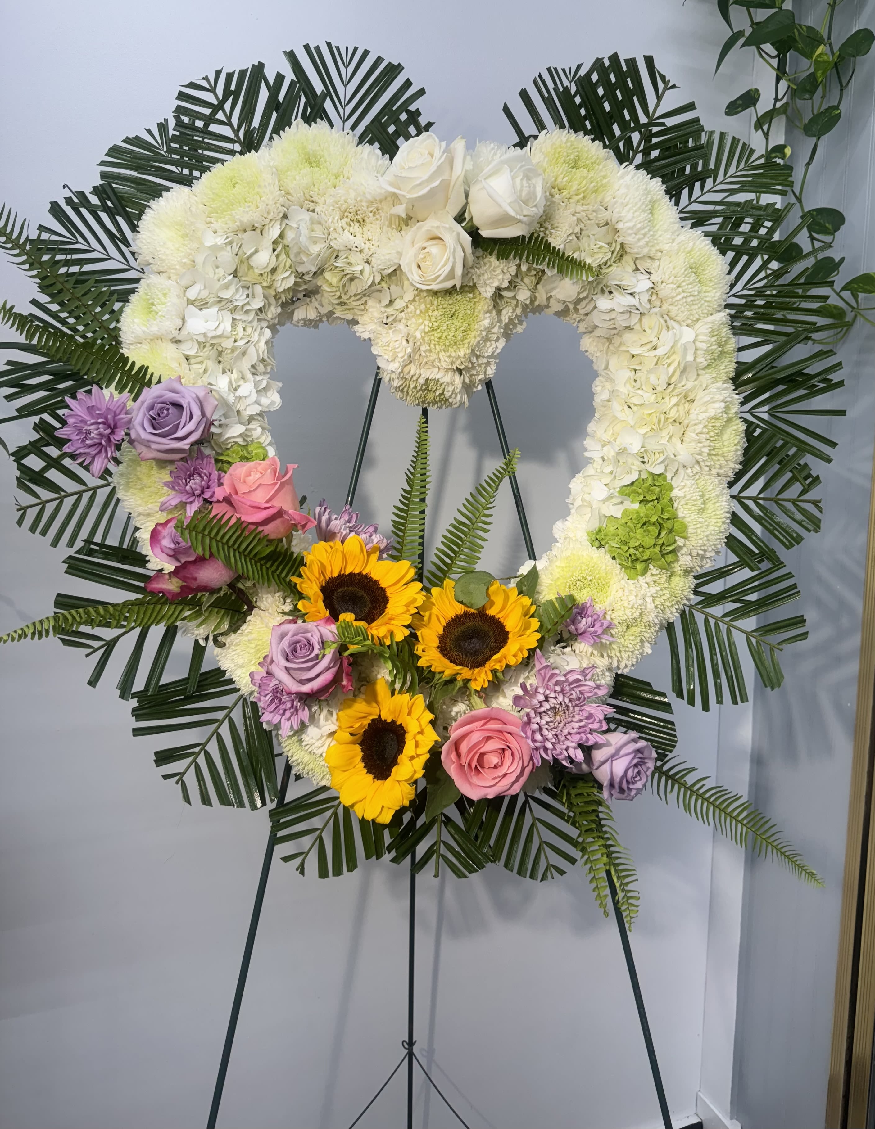 Heart-shaped floral wreath on an easel with white, pink, purple, and yellow flowers