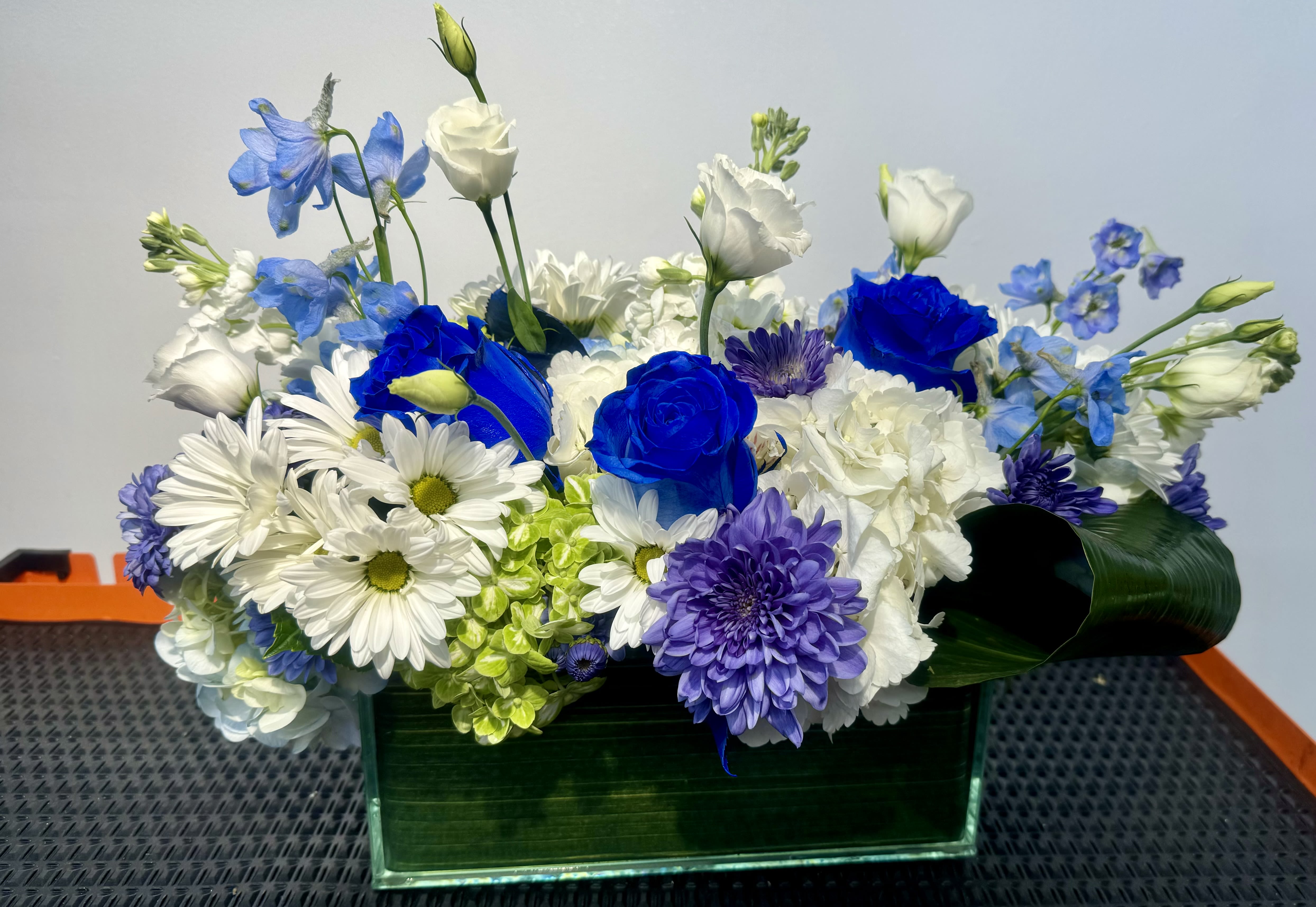 Blue, white, and purple flowers arranged in a rectangular glass vase
