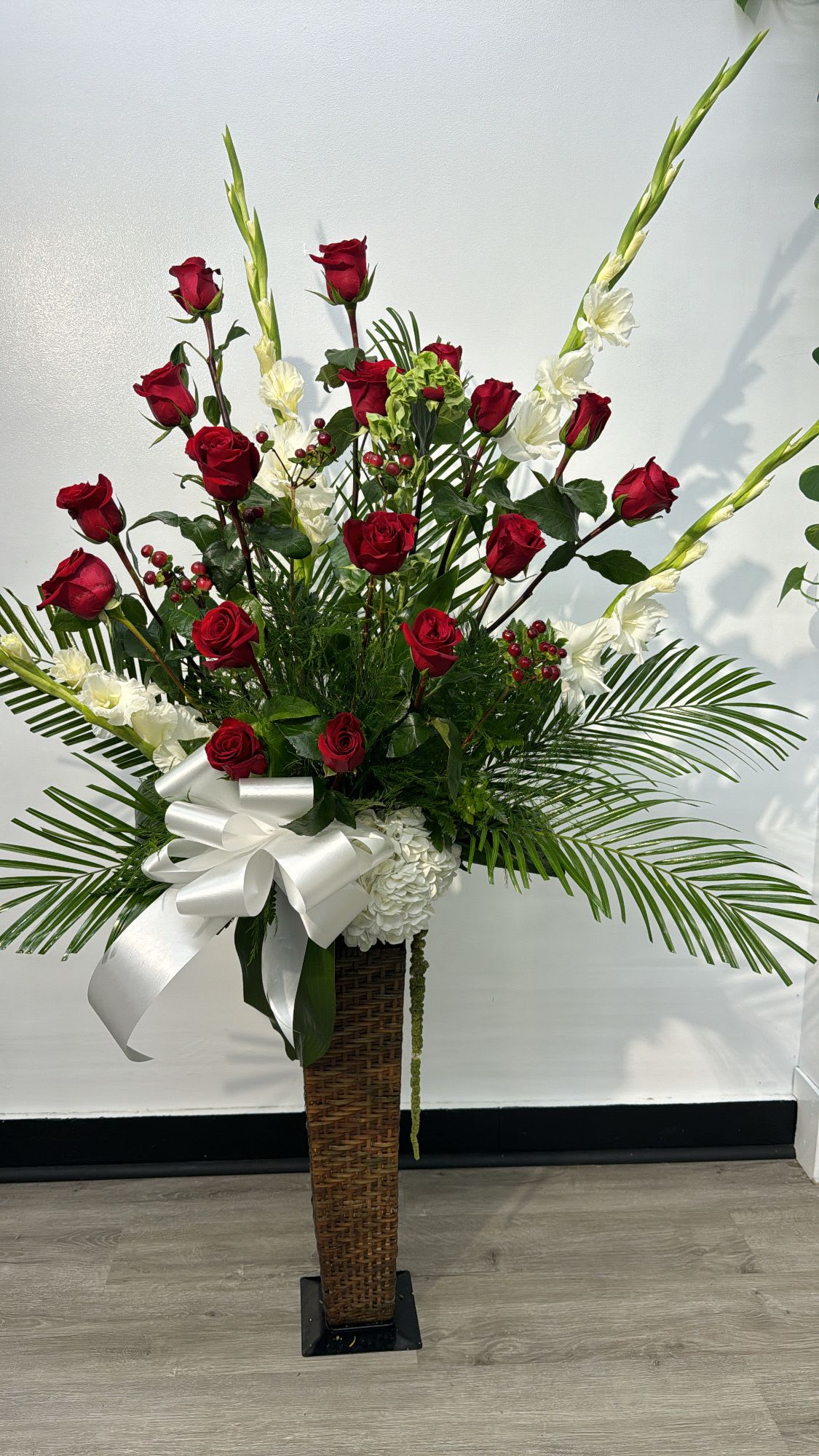 Tall floral arrangement with red roses and white flowers in a wicker pedestal vase