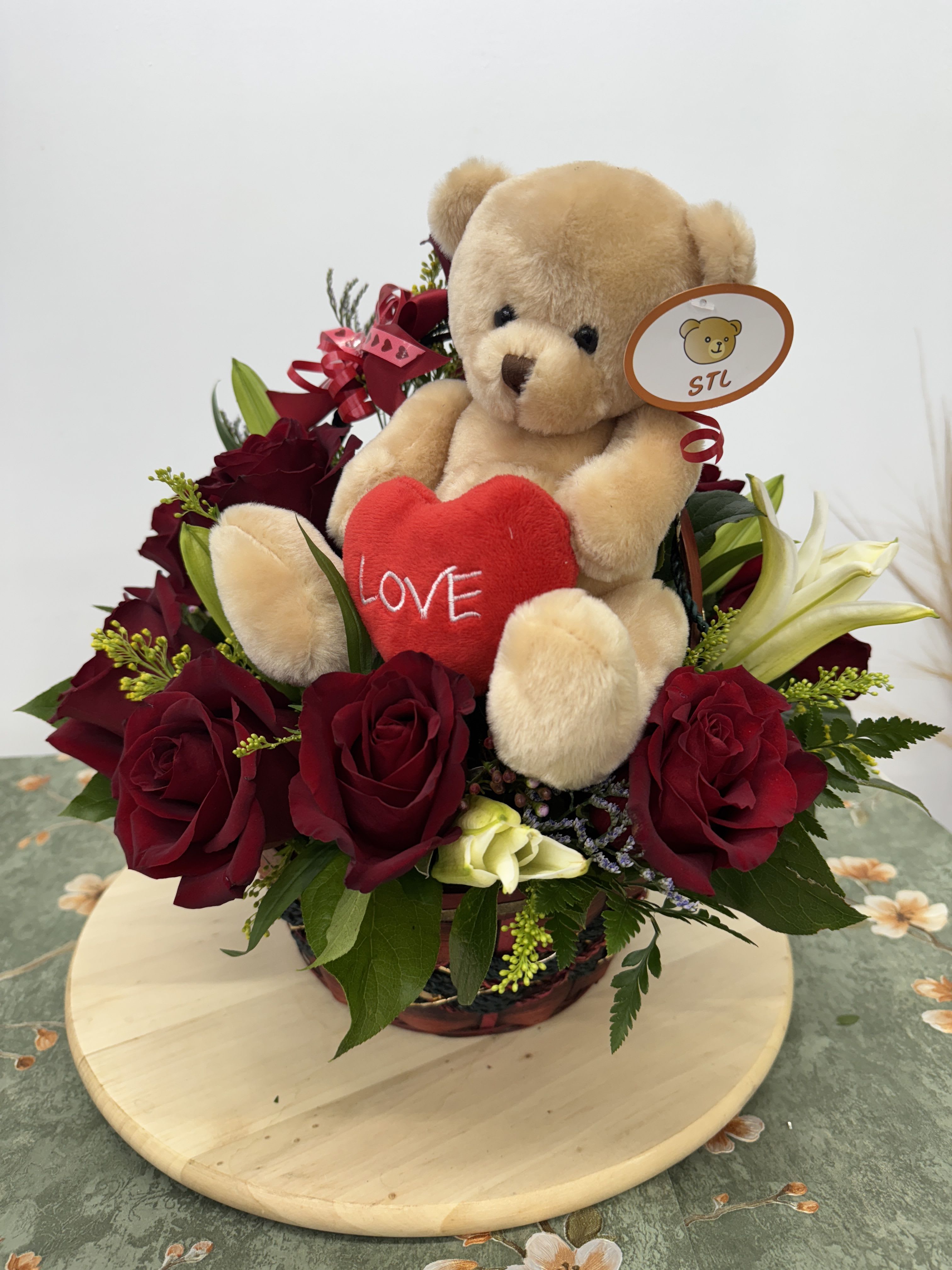 Teddy bear with a red heart surrounded by red roses in a basket