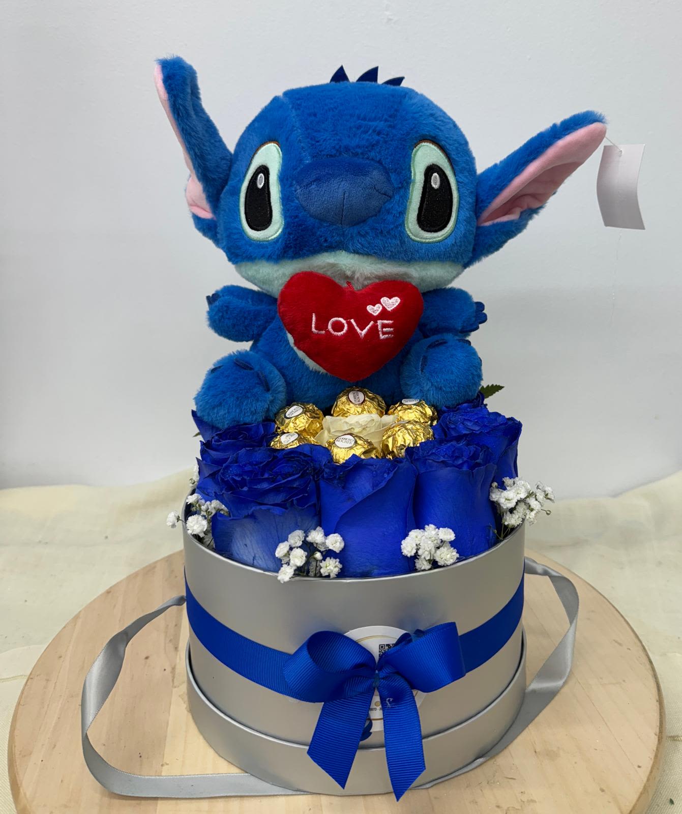 Blue plush character in a gift box with roses and chocolates