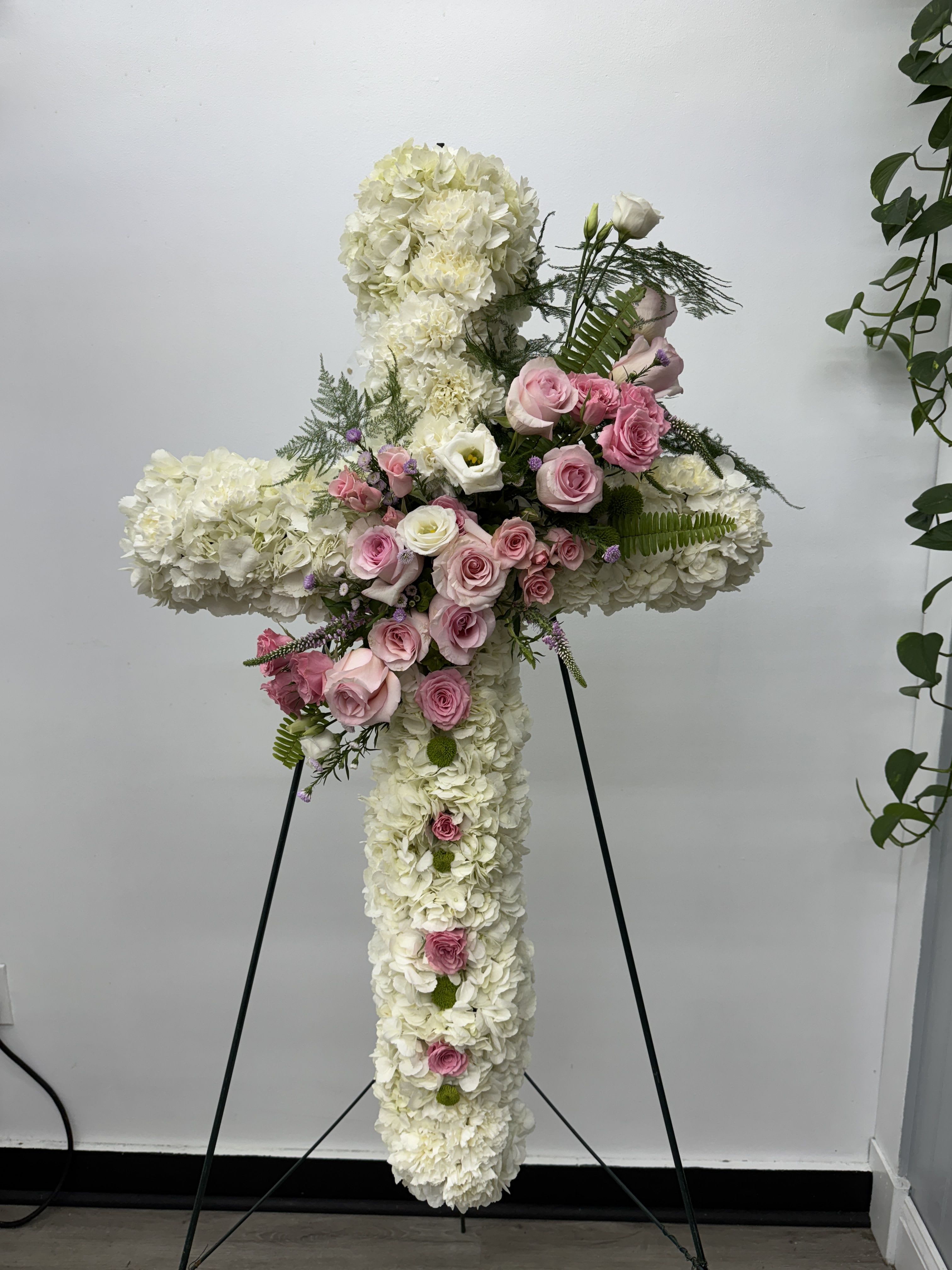 Large white floral cross with pink roses on a stand
