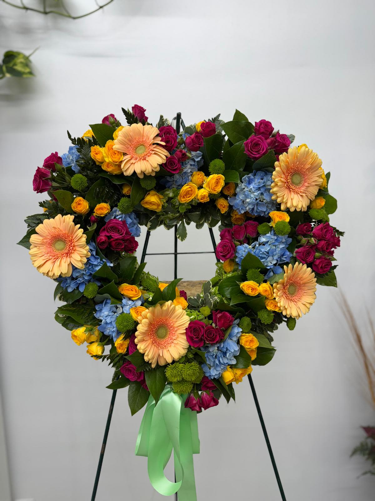 Heart-shaped floral wreath with roses, gerberas, and hydrangeas on a stand