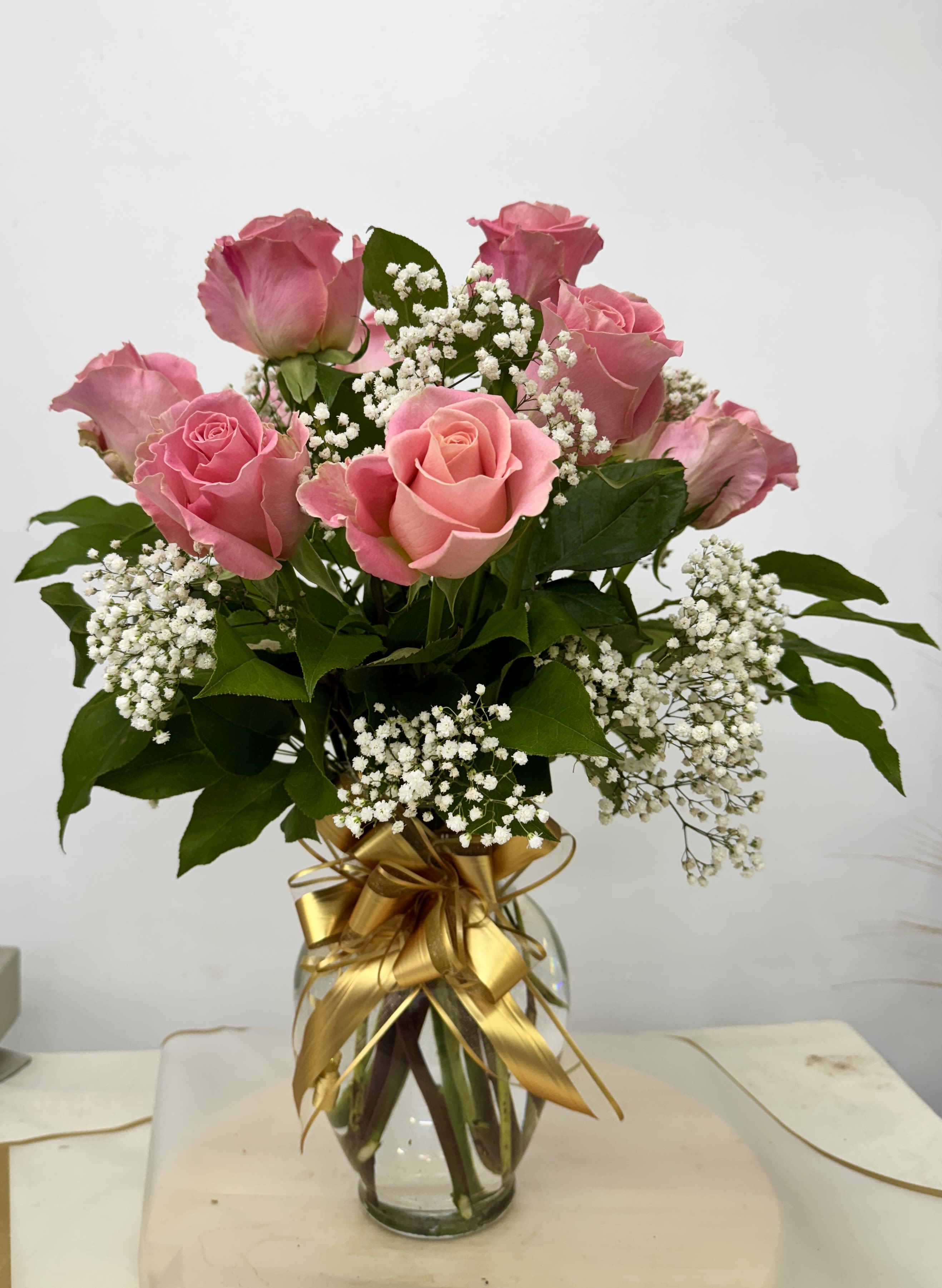 Pink roses in a glass vase with white baby's breath and a gold ribbon