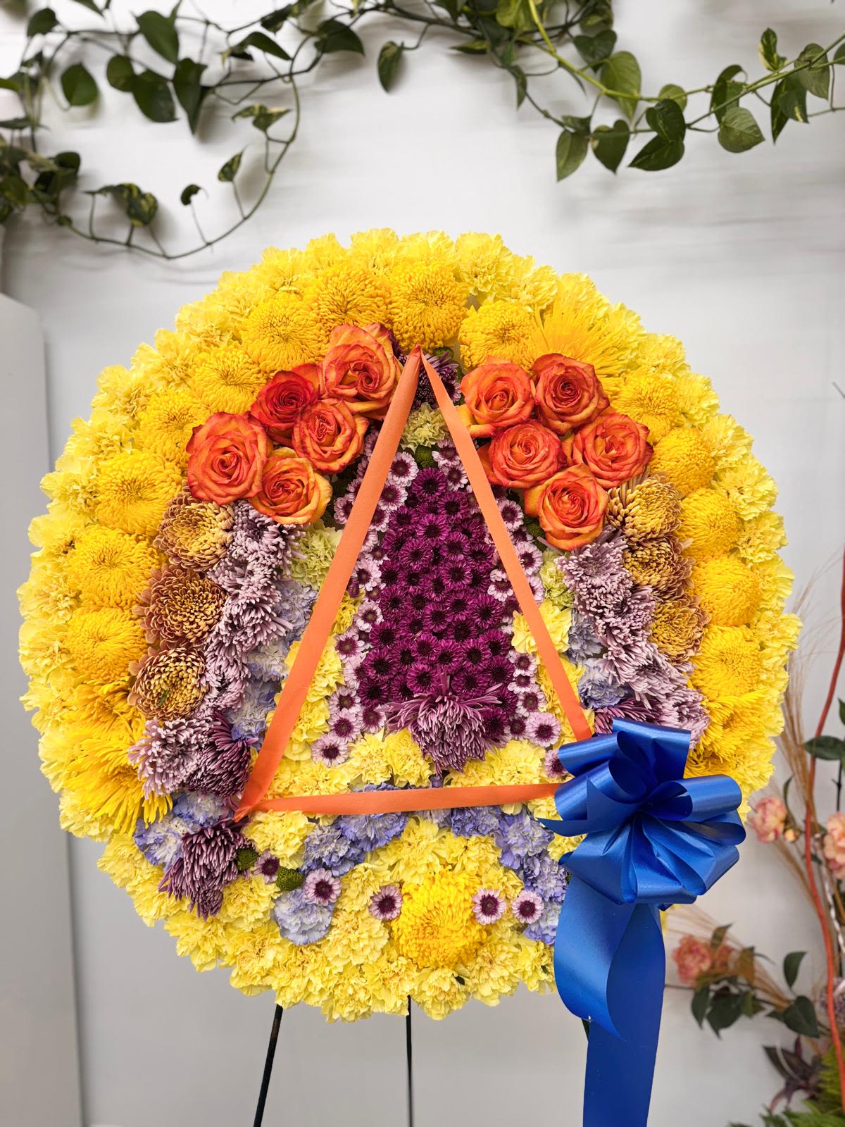 Large floral wreath with yellow, orange, and purple flowers and a blue ribbon