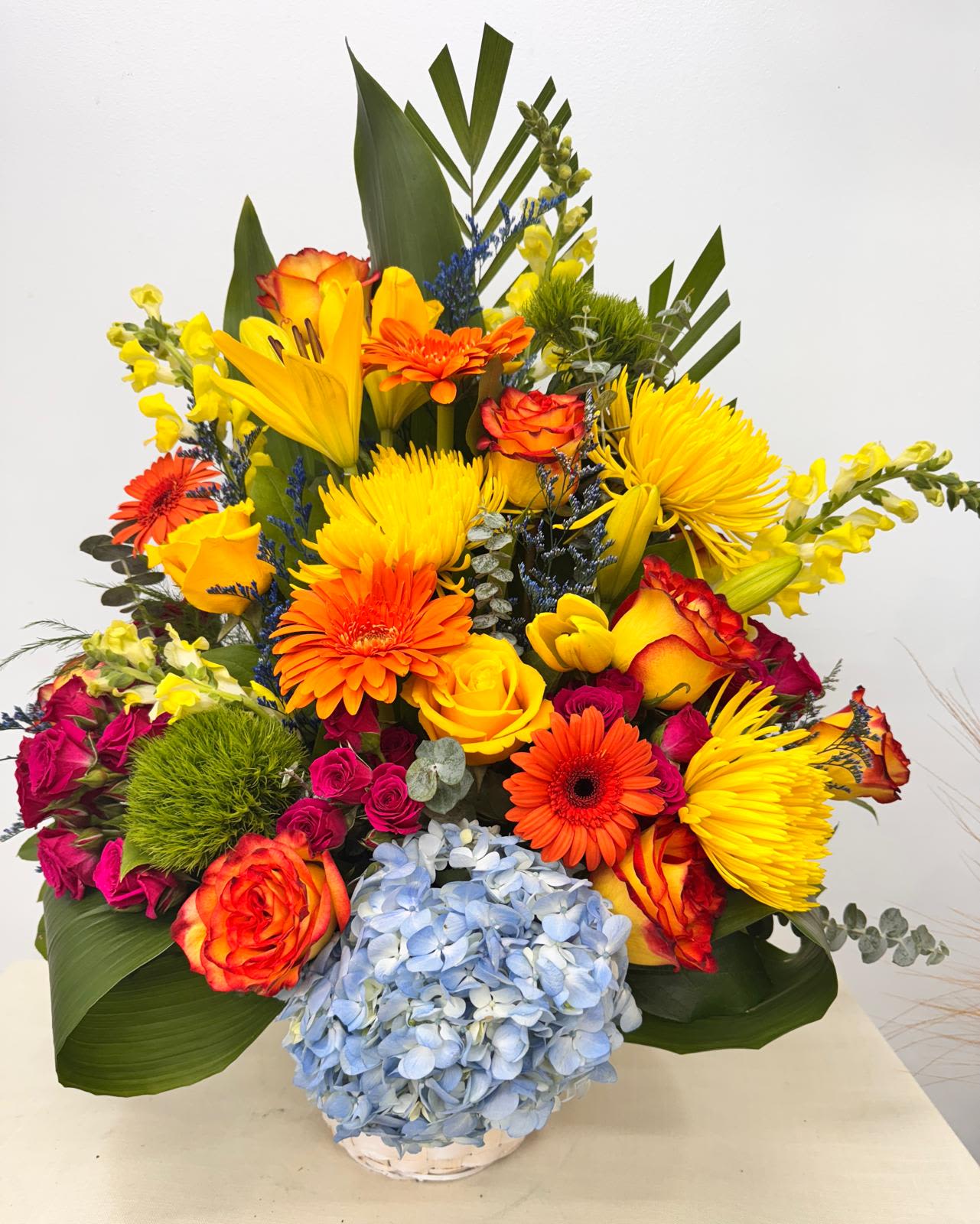 Bright mixed bouquet with roses, gerberas, lilies, and blue hydrangea in a vase
