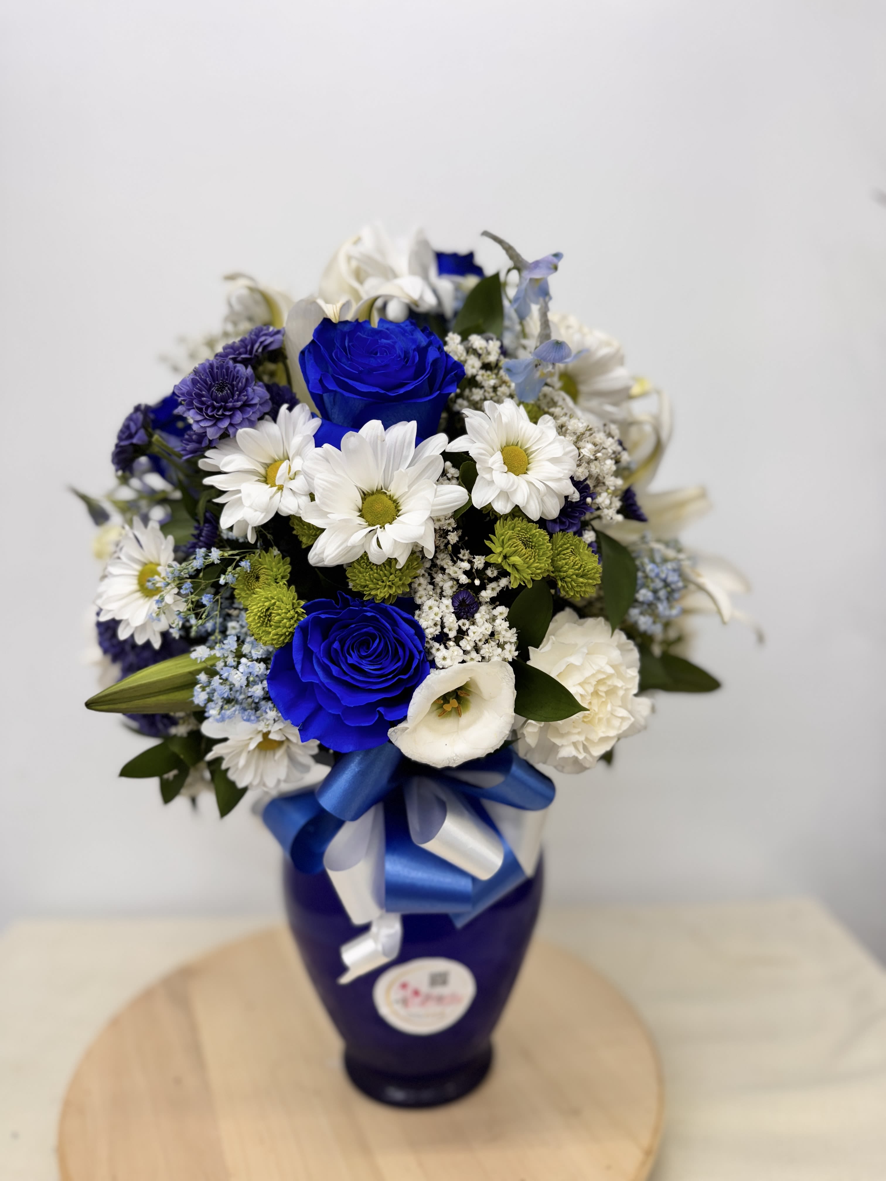 Blue and white flower bouquet in a dark vase with a ribbon