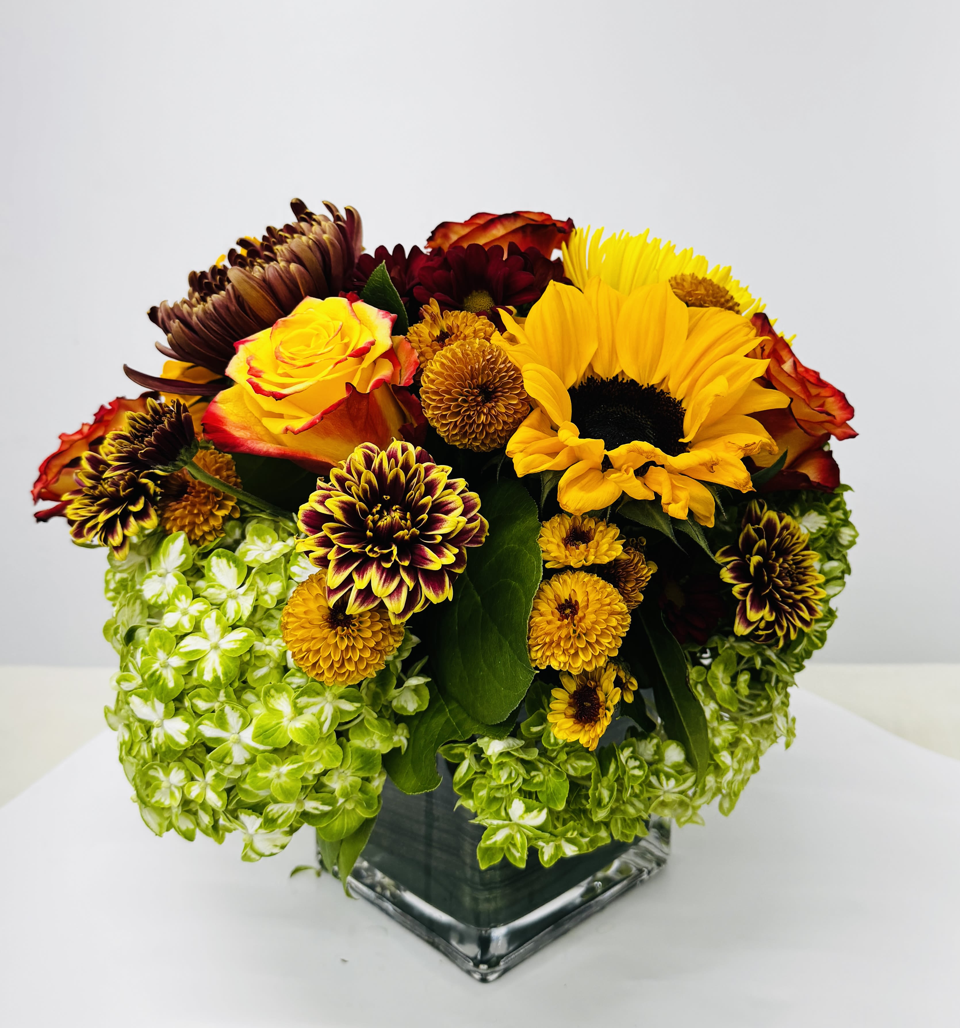 Bouquet of yellow and burgundy flowers in a square glass vase