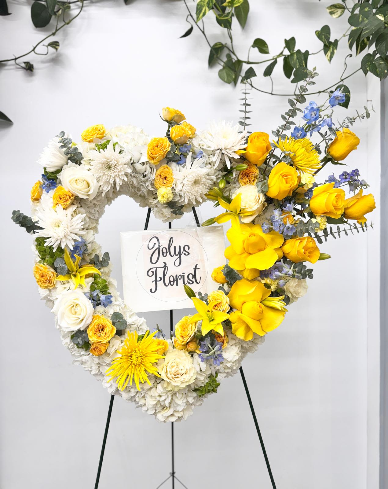 Heart-shaped floral wreath on an easel with yellow and white flowers