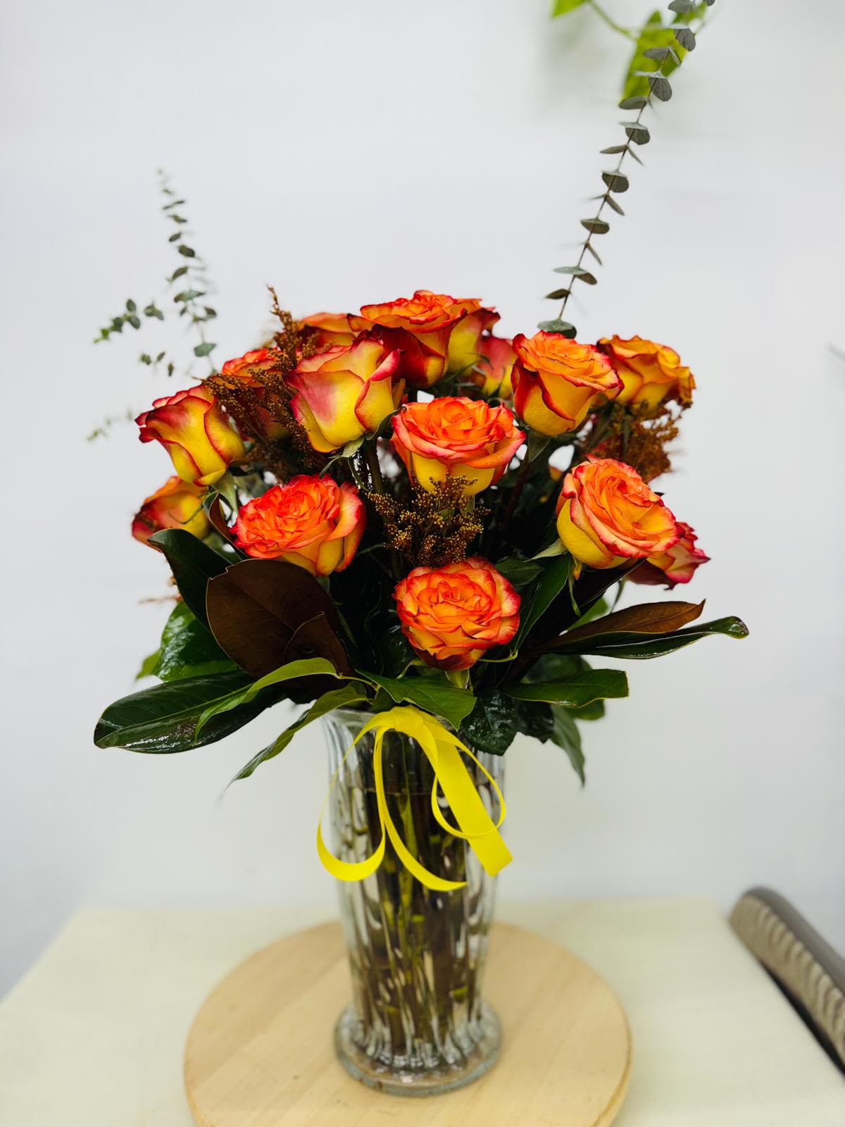 Bouquet of orange and yellow roses in a clear glass vase with a yellow ribbon