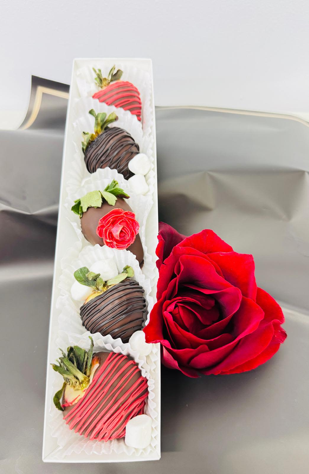 Box of chocolate-covered strawberries beside a red rose