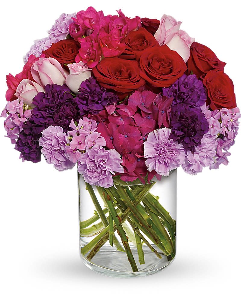 Bouquet of red roses, pink hydrangeas, and purple carnations in a clear glass vase
