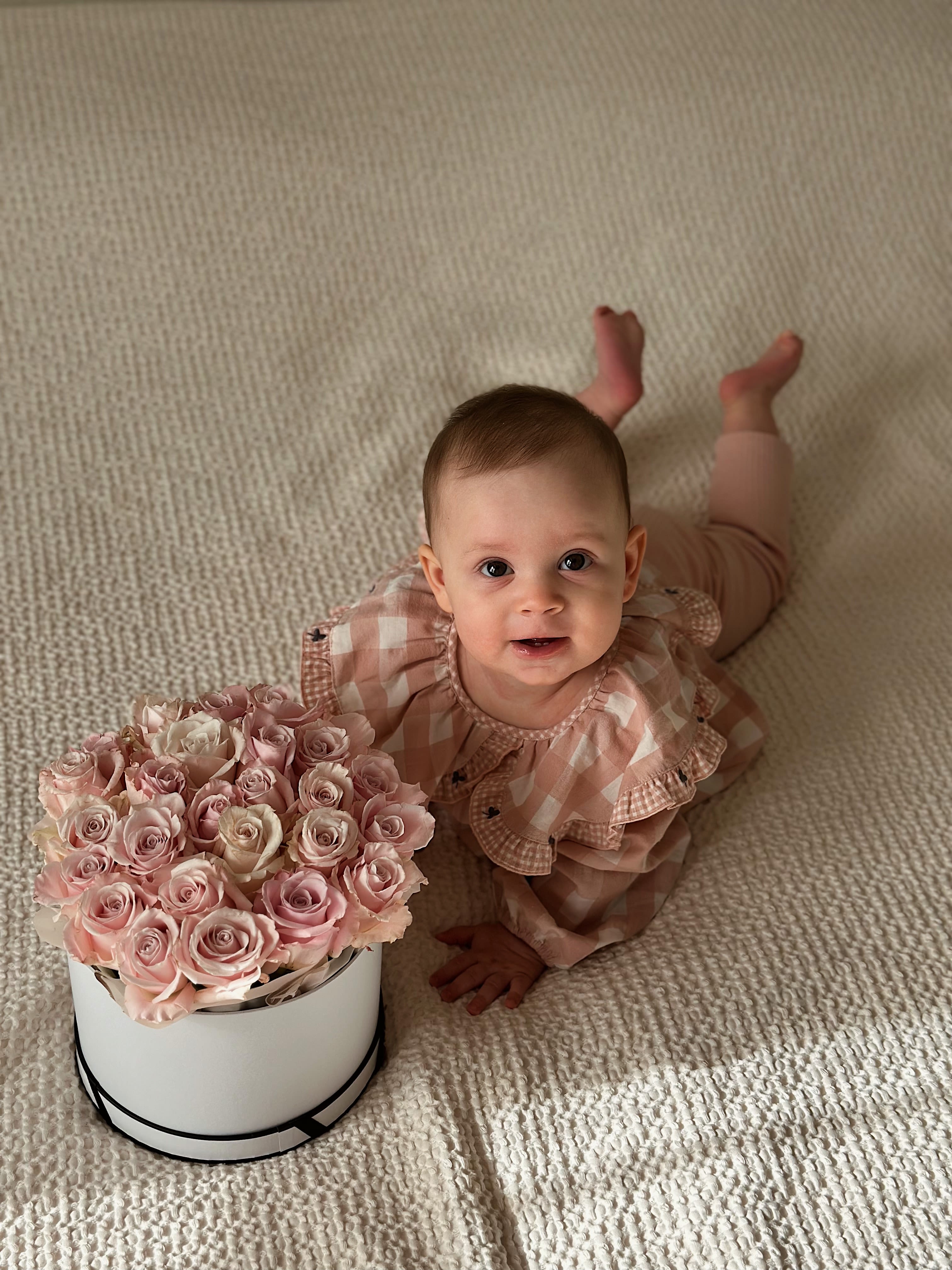Baby beside a box of pale pink roses on a carpet