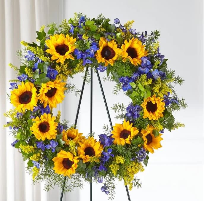 The beautiful Sunflowers Wreath - The beautiful sunflowers in our Bright Rays S offers a display of admiration, loyalty and hope. Each bright bloom is complemented by lush greens and blue delphinium blooms. Their uplifting nature reminds loved ones of your support and the brighter days ahead as they navigate through a difficult time.