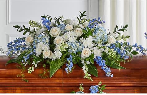 Blessings of Memory half casket cover - Featuring soothing tones of blue and white, the traditional arrangements of this sympathy  are meant for celebrating the life of a loved one at a visitation, funeral, church service, cremation, or cemetery service – or as a delivery to the family's home.Honor a life so beautifully lived with a proud display of blue and white blooms. OurHonor a life so beautifully lived with a proud display of blue and white blooms. Our half casket cover, crafted with care and artistry by our expert florists with blue delphinium, white roses, and accented with a blue satin ribbon, is an unforgettable way to commemorate a lifetime of loving devotion., crafted with care and artistry by our expert florists with blue delphinium, white roses, and accented with a blue satin ribbon, is an unforgettable way to commemorate a lifetime of loving devotion.