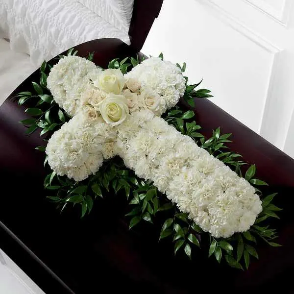 Peaceful Memories Casket Spray Cross  - The Peaceful Memories Casket Spray is a gorgeous way to commemorate the faith and devotion of the deceased. White carnations are arranged in the shape of a cross accented in the middle with white roses and spray roses and along the sides with lush greens to create a lovely casket spray that brings peace and solace to those that attend their final farewell.