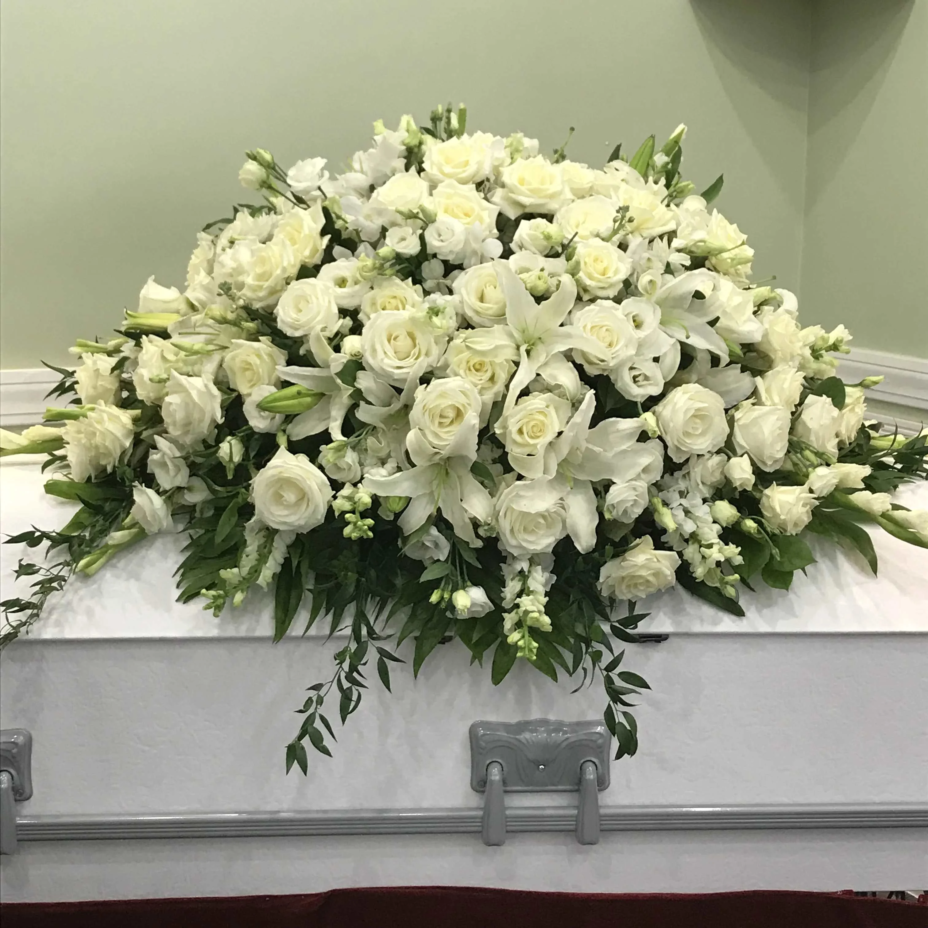 Honor a life Casket Spray - Honor a life so beautifully lived with a proud display of Half casket cover arrangement of white roses, hybrid lilies, , Snapdragons, Lisianthus, with greeneries