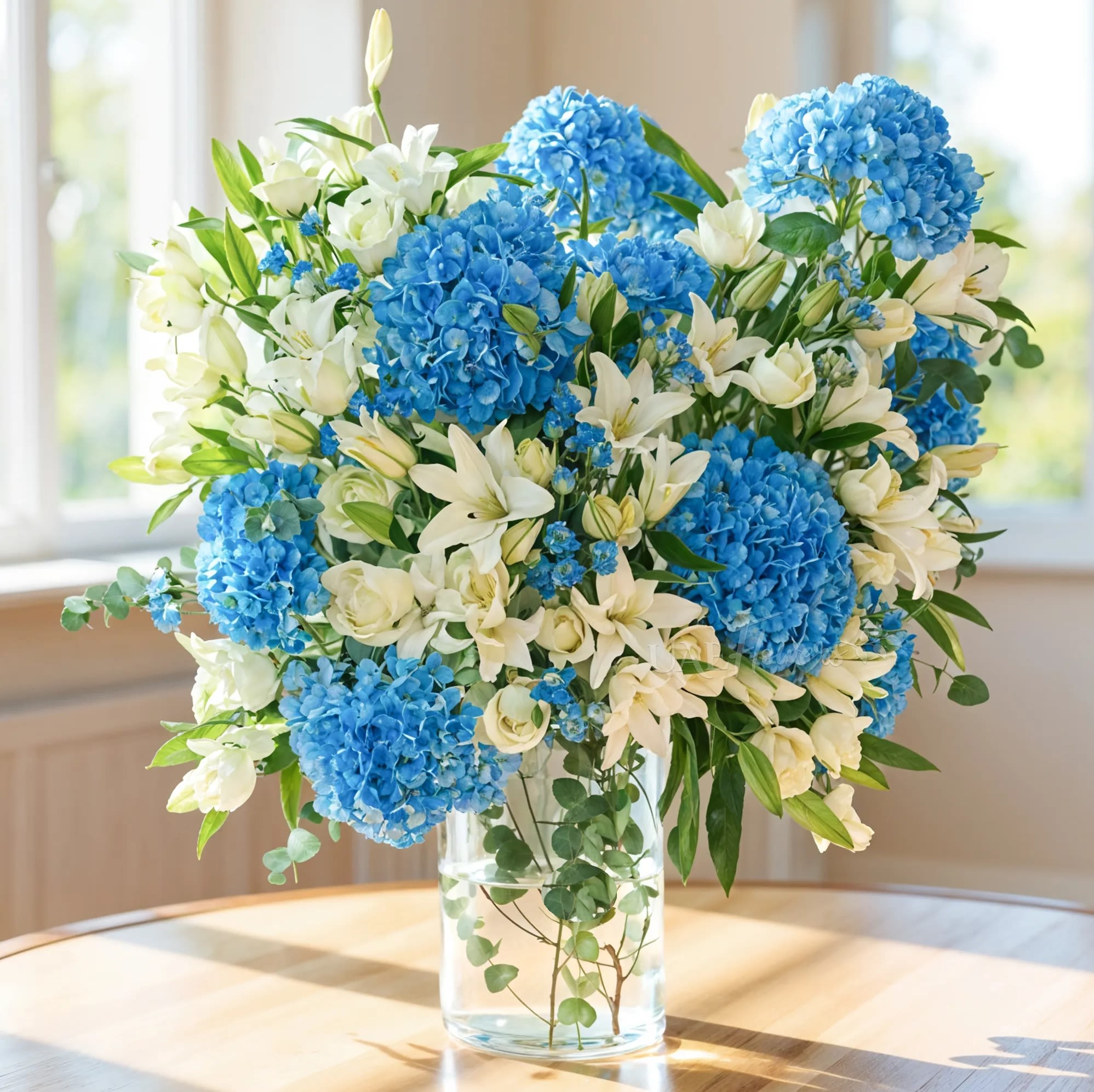 Blue hydrangeas and white lilies in a clear glass vase