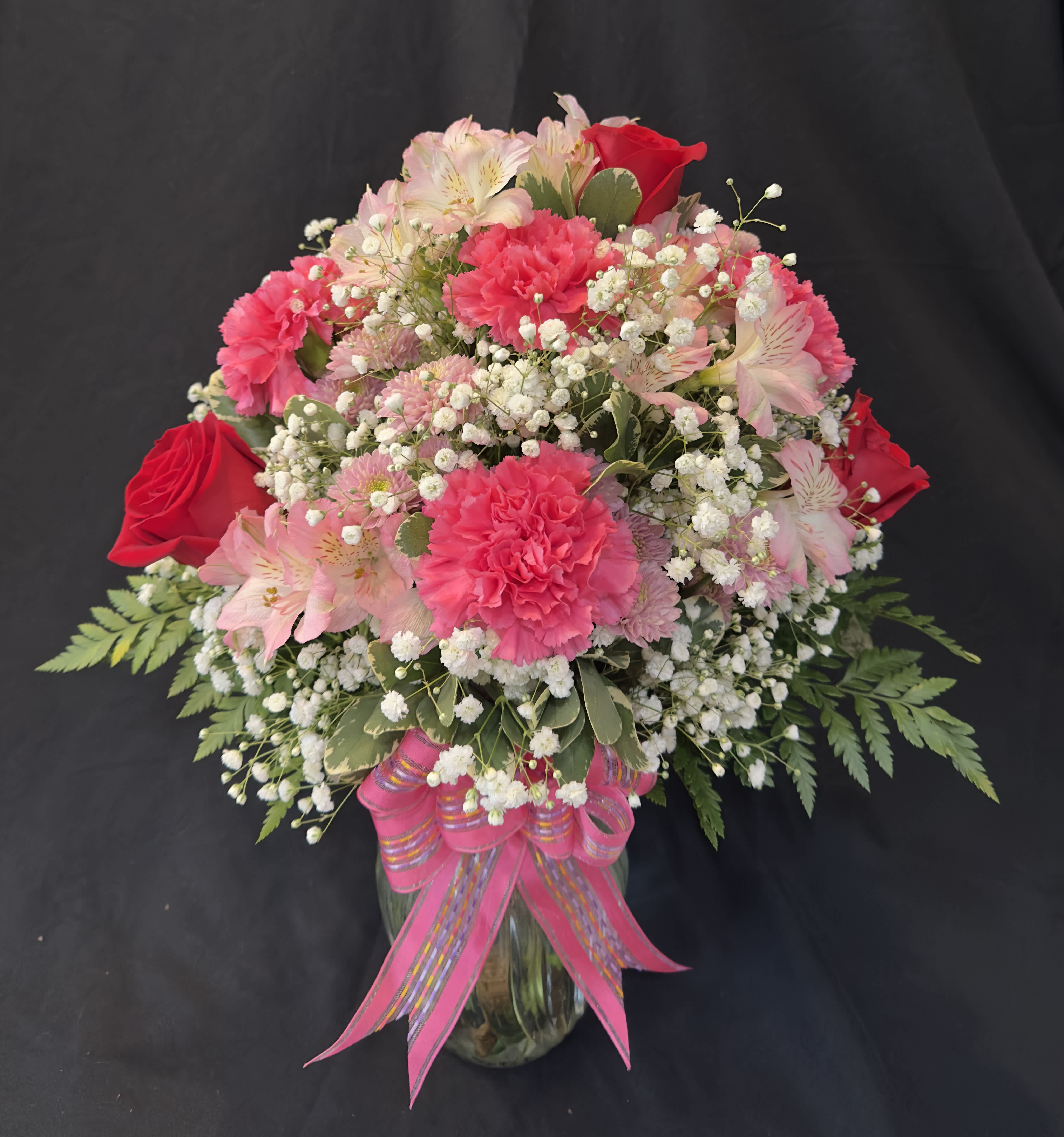 Pink and red flower arrangement in a glass vase with a pink ribbon