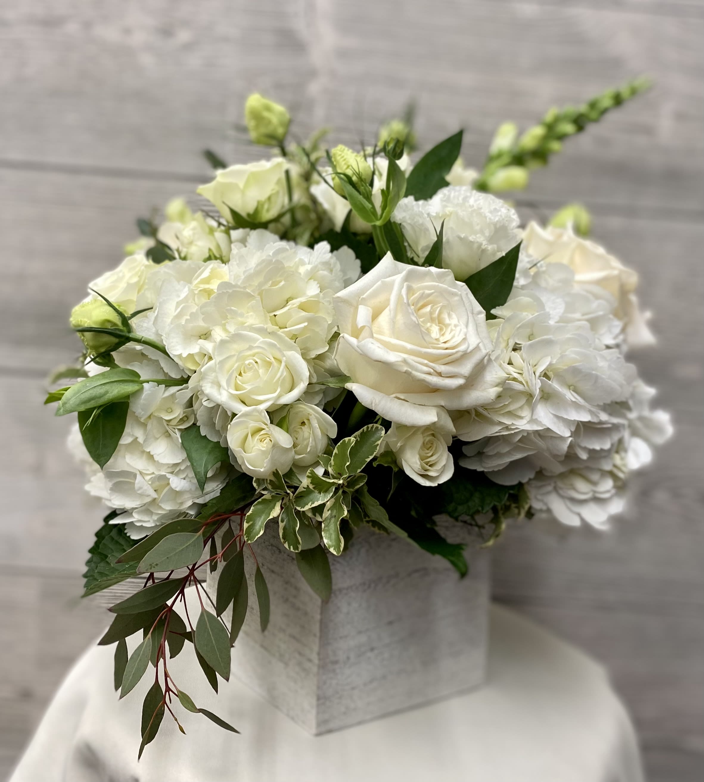 White roses and hydrangeas arranged in a square box with greenery