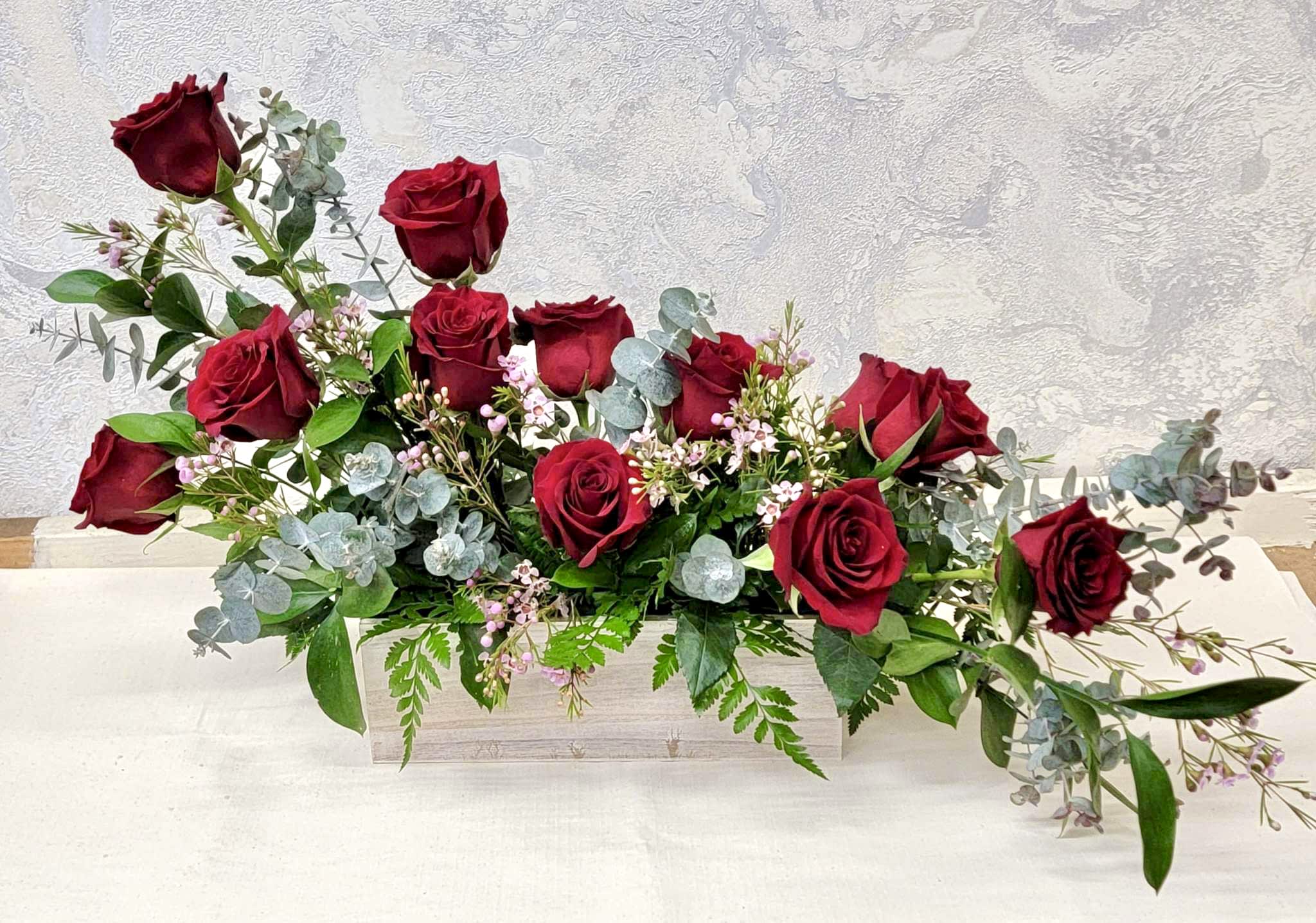 Low rectangular centerpiece of red roses with pink blossoms and eucalyptus in a wooden box