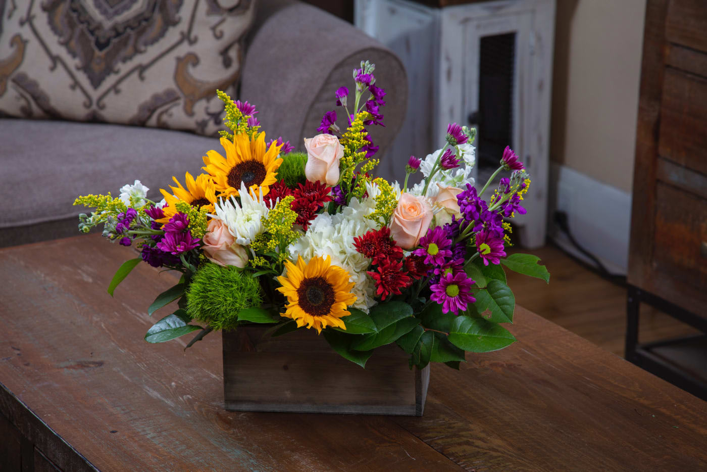 Mixed bouquet with sunflowers, roses, and purple blooms in a wooden box