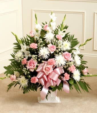 Pink roses and white flowers arranged in a vase with a pink ribbon