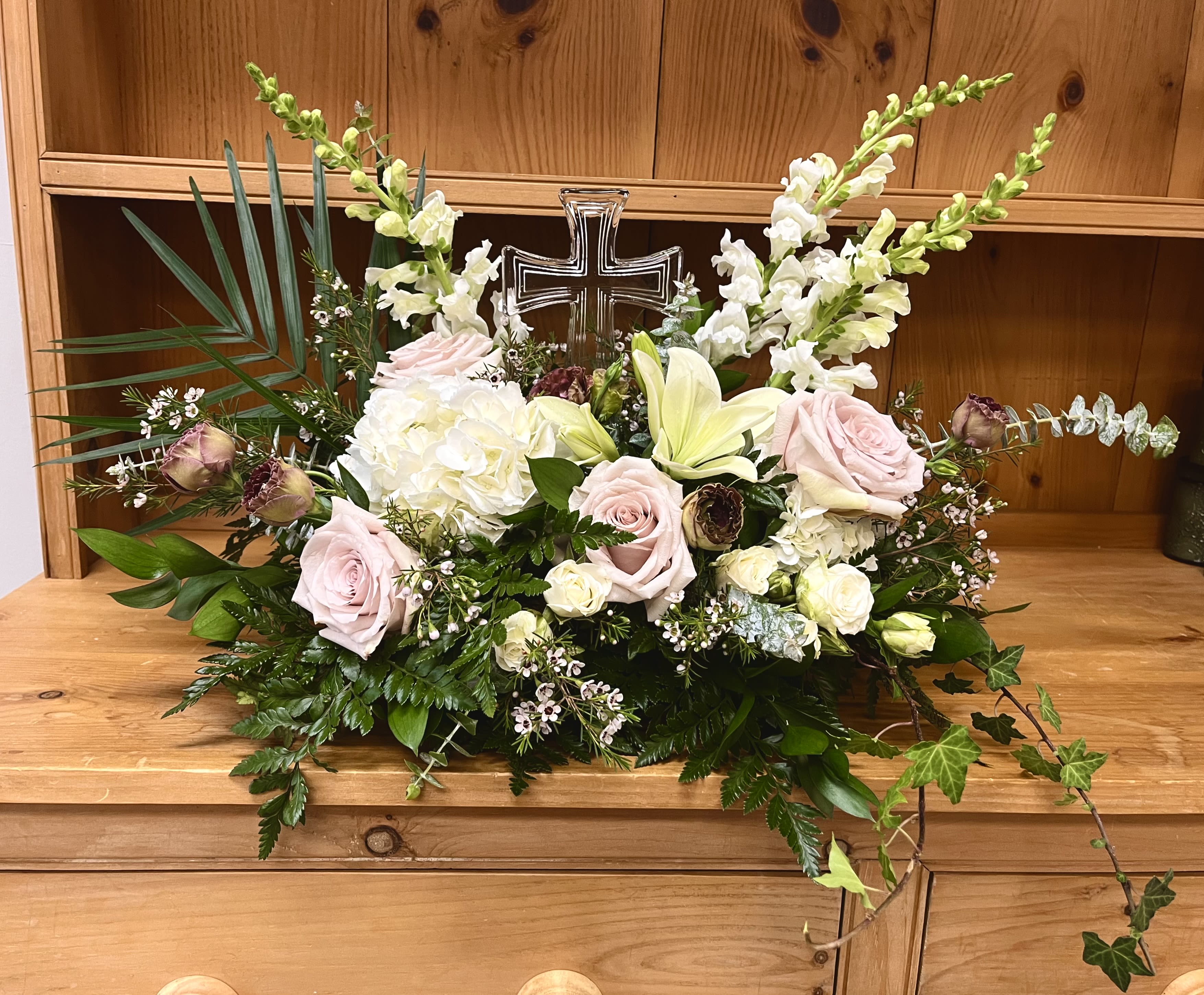 Pastel floral arrangement with roses, lilies, and a cross centerpiece