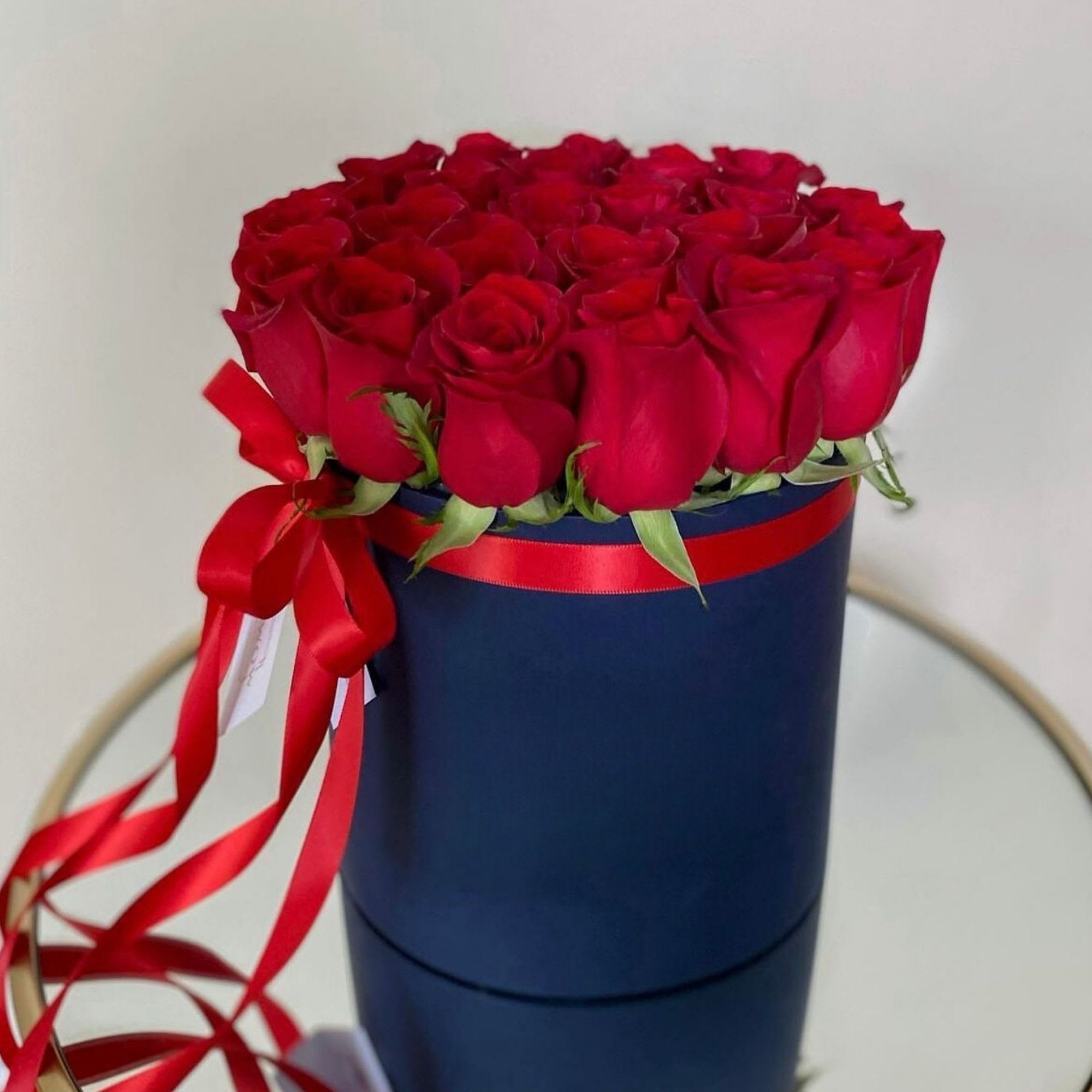 Red roses arranged in a navy round box with a red ribbon