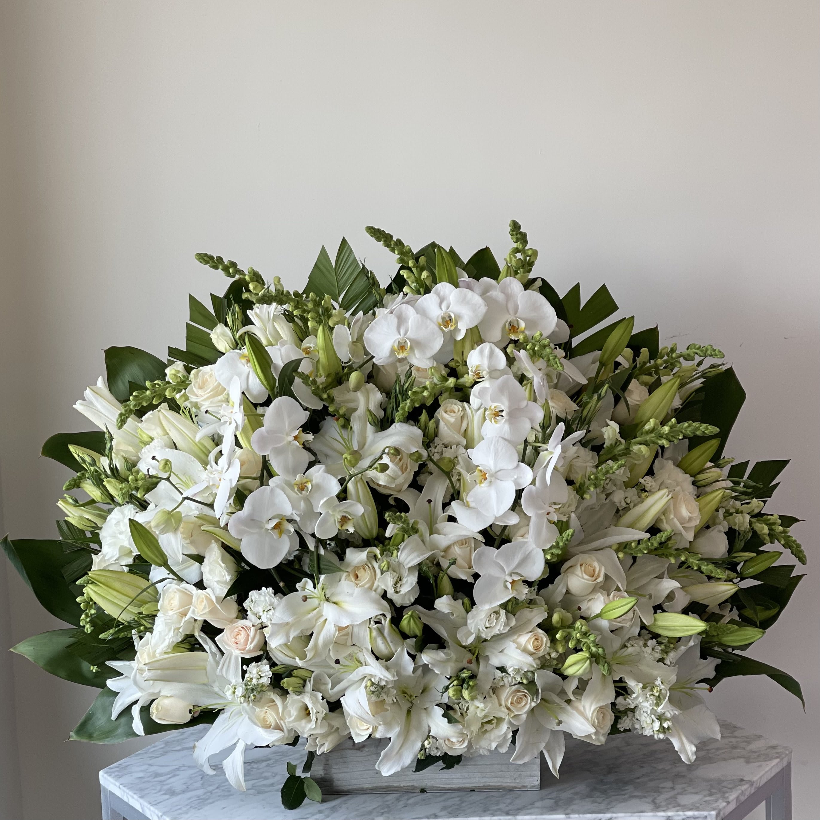 Large white floral arrangement with orchids and lilies in a low container
