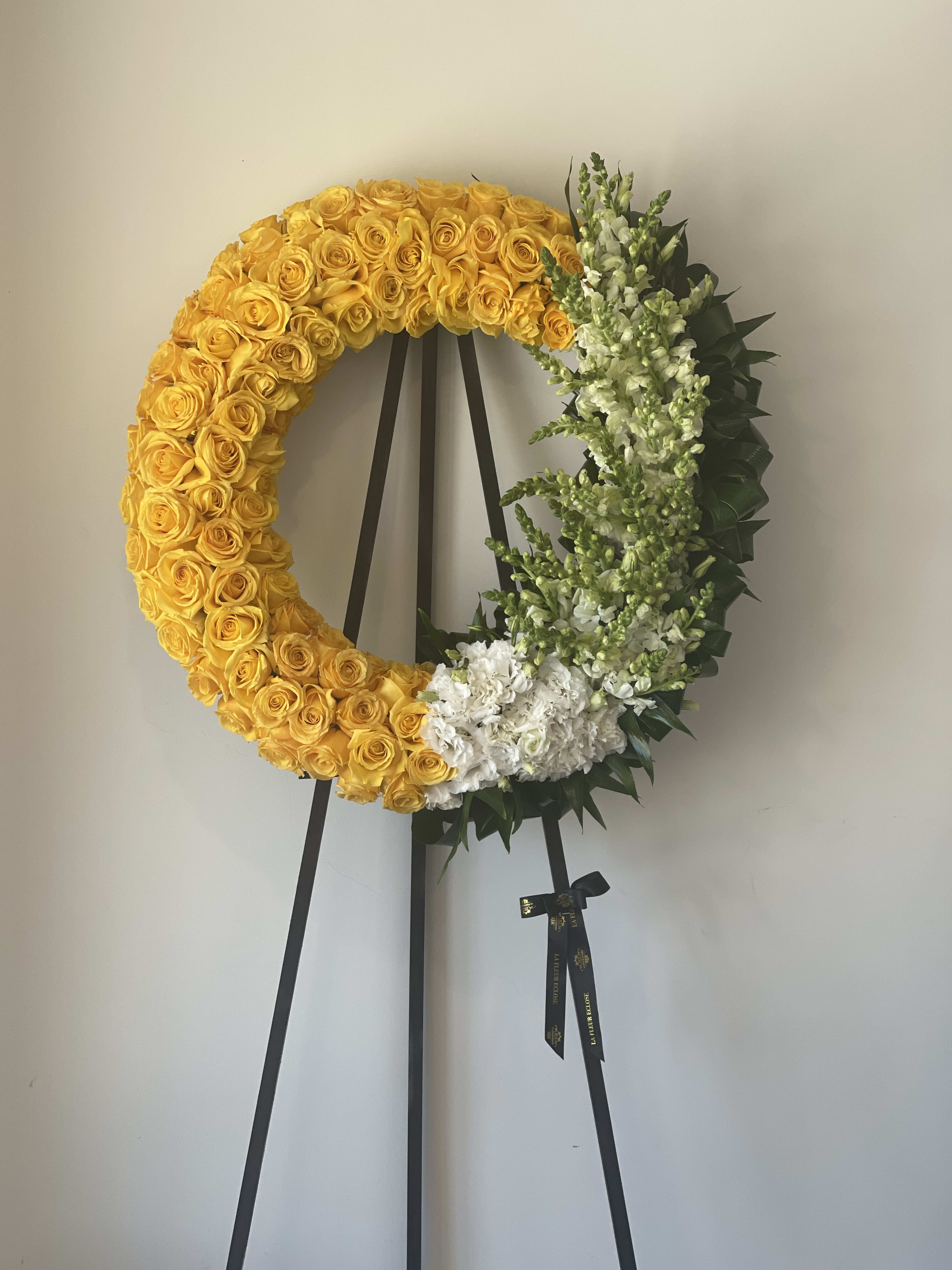 Yellow rose wreath on a black easel with white flowers and greenery